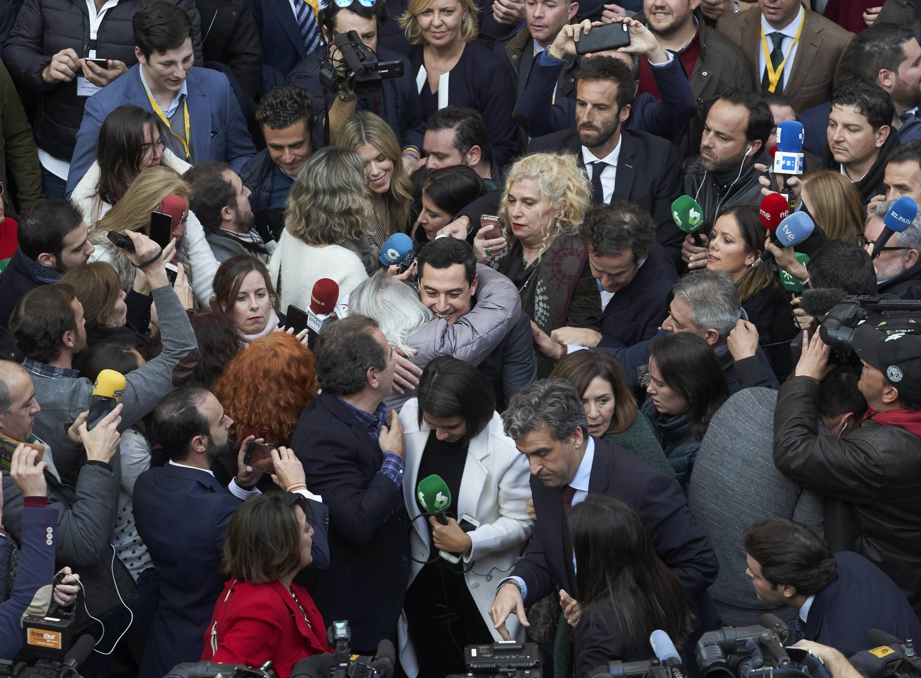 Juanma Moreno (PP), en el centro, recibe felicitaciones rodeado de periodistas tras el debate de investidura en el Parlamento de Andalucia en 2019.
