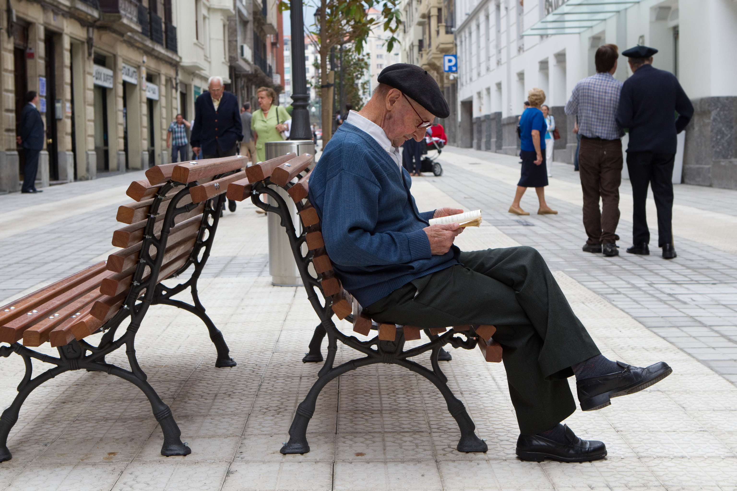 Un hombre lee un libro en una calle peatonalizada.