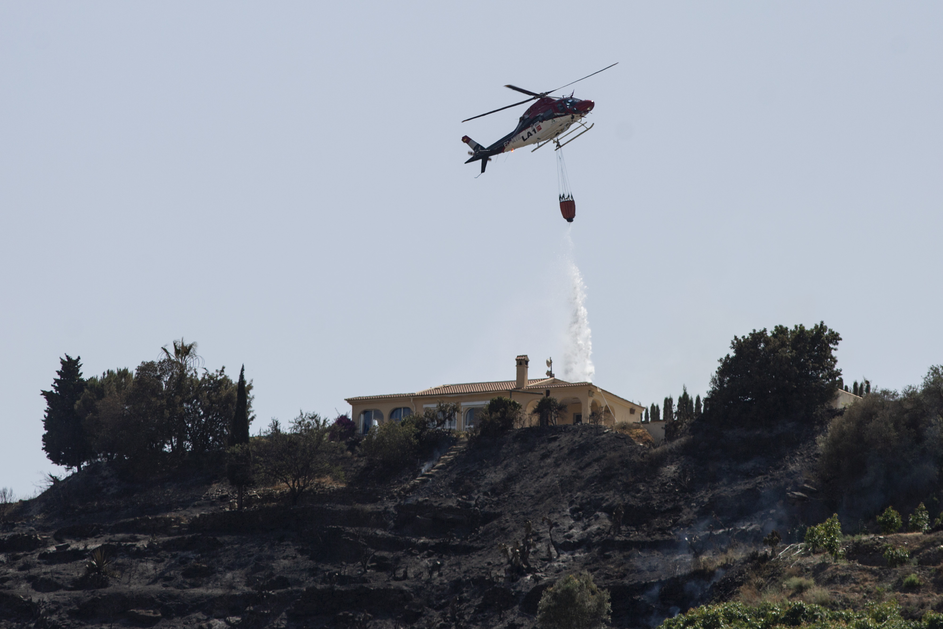 Un helicptero descarga agua sobre una vivienda en peligro en el incendio de Pujerra.