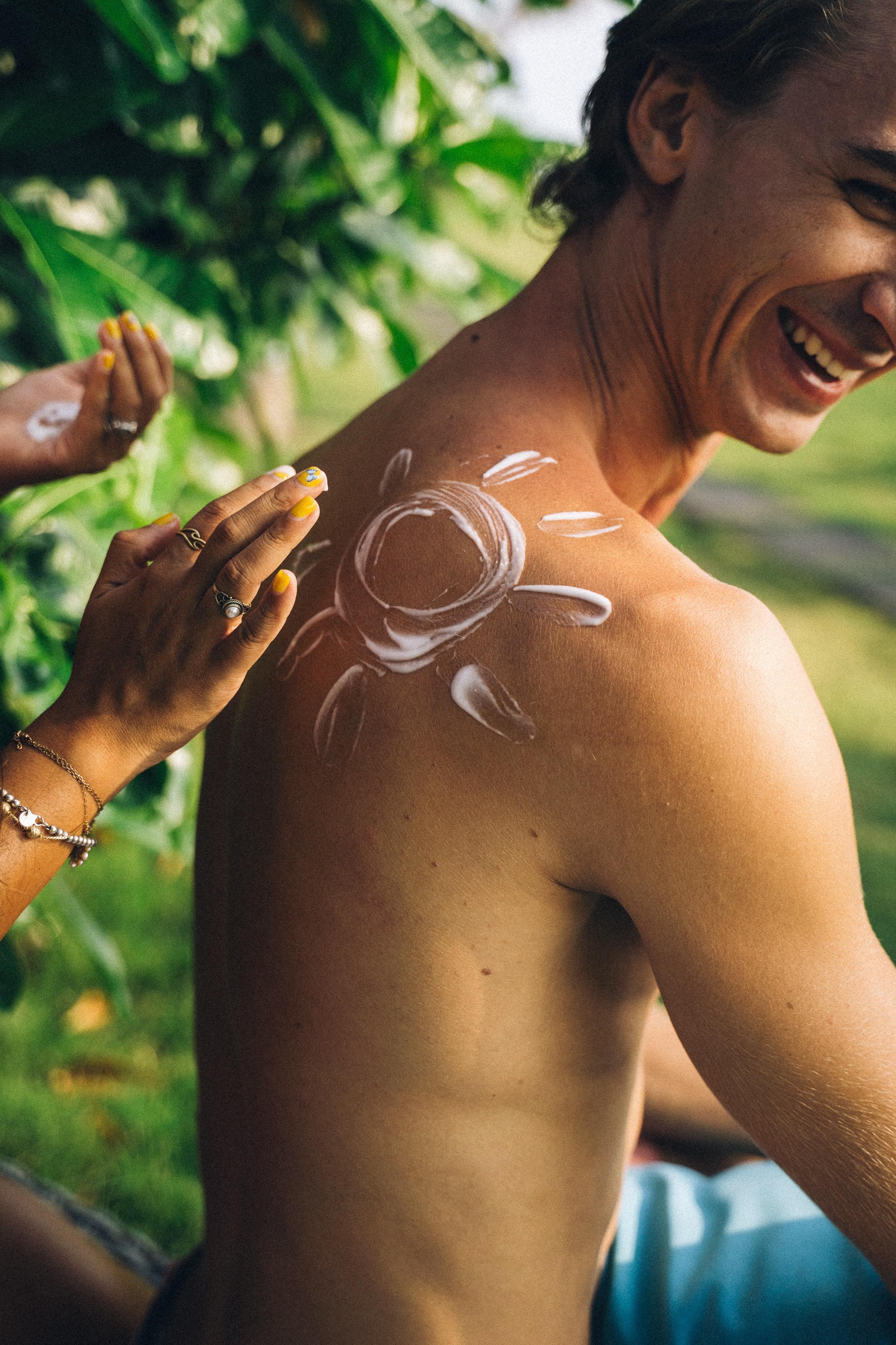 Un hombre recibe crema solar en la espalda con un sol dibujado.