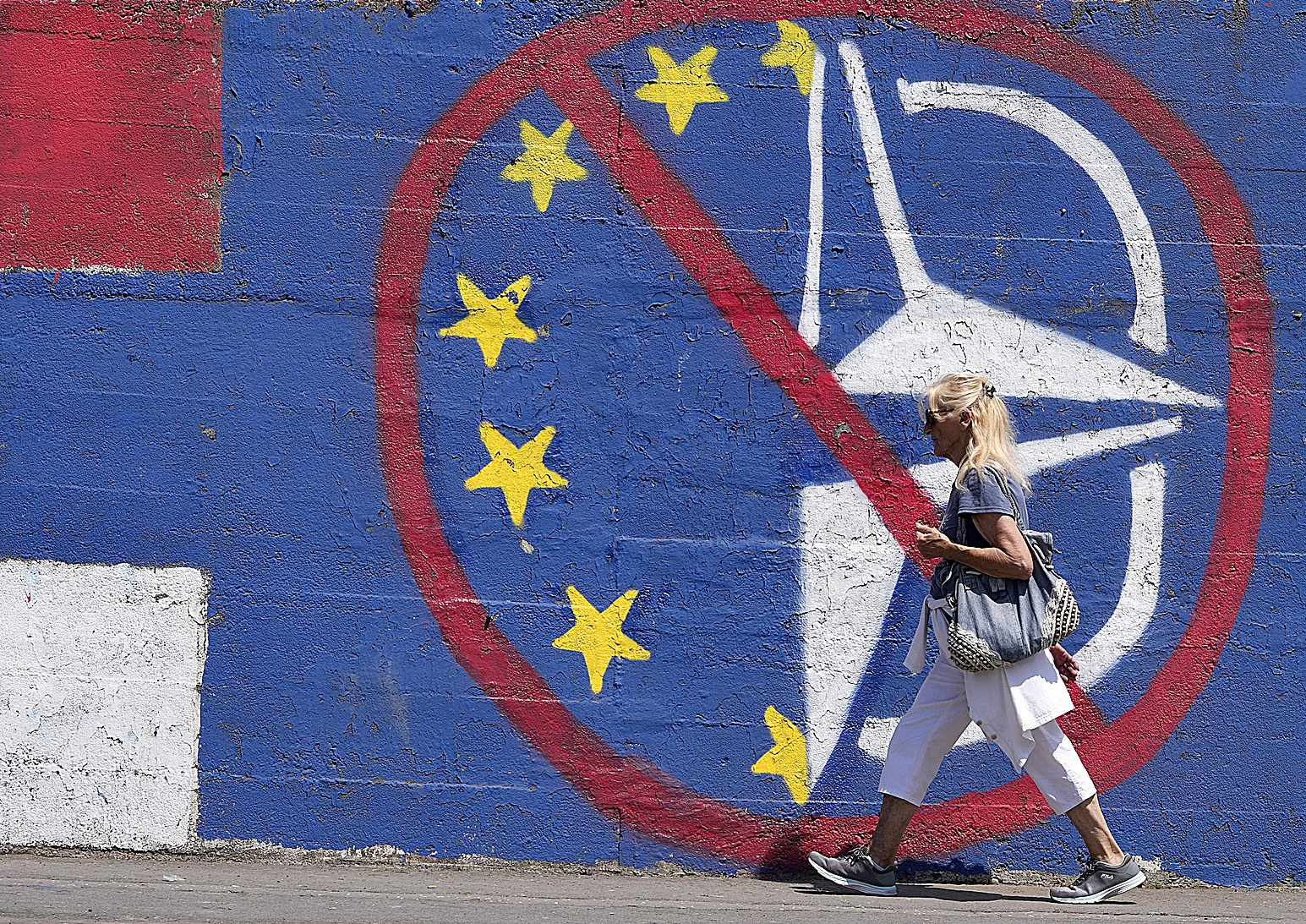 Una mujer camina junto a un grafiti contrario a la OTAN.