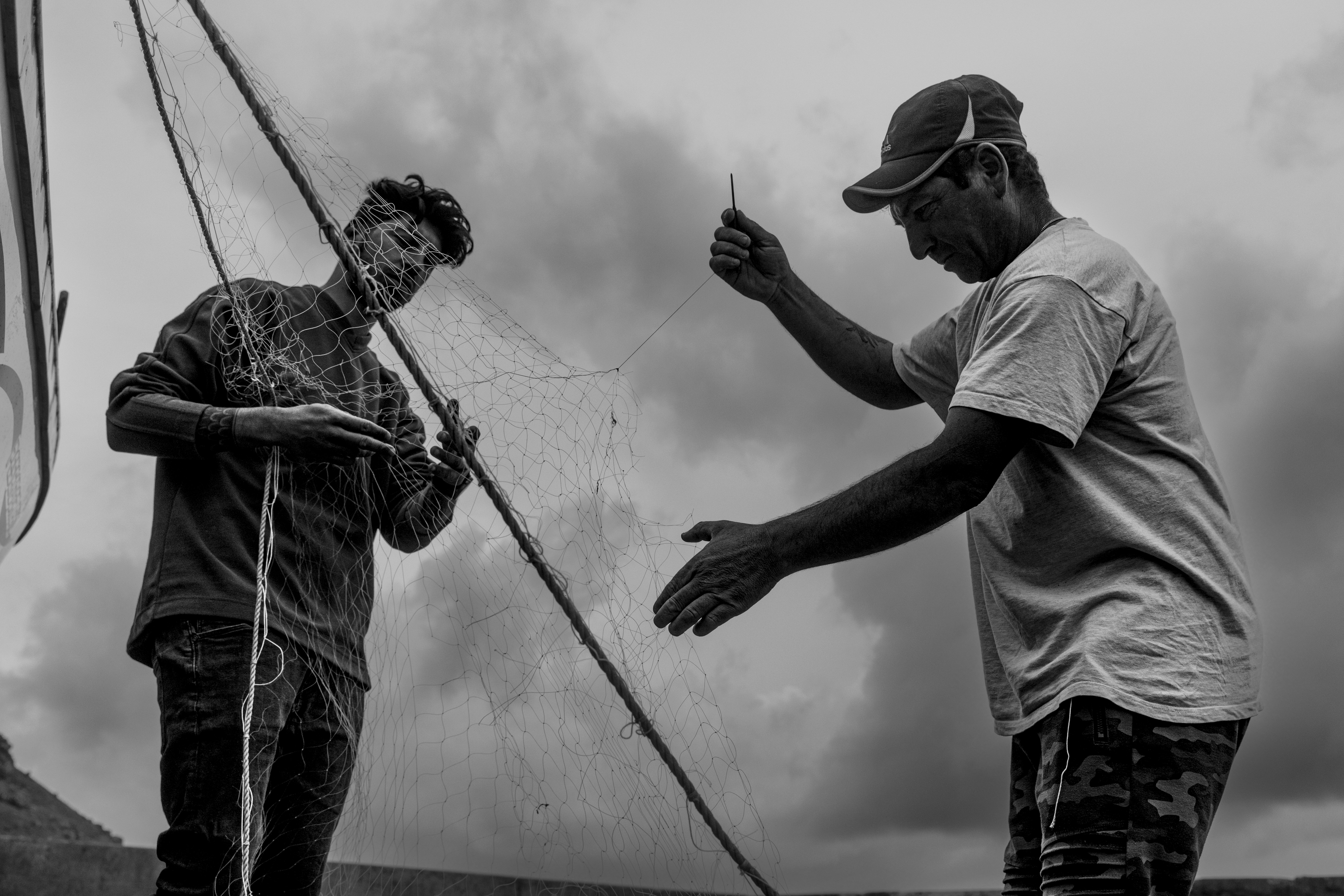 Dos pescadores, padre e hijo, reparando las redes en un día de mala mar.