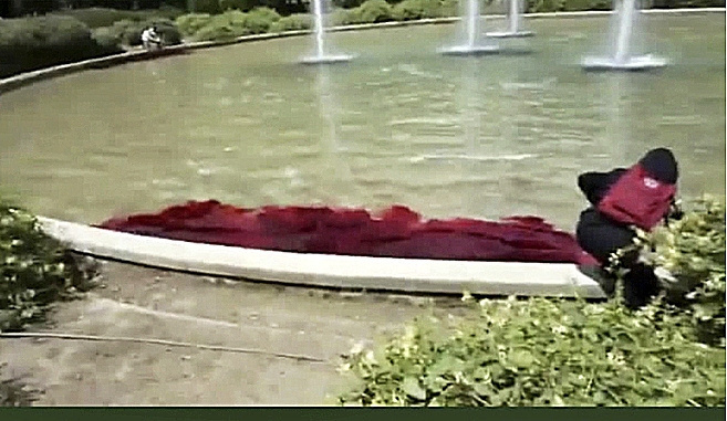 Uno de los activistas lanzando un lquido rojo en una fuente del parque de la Guindalera.