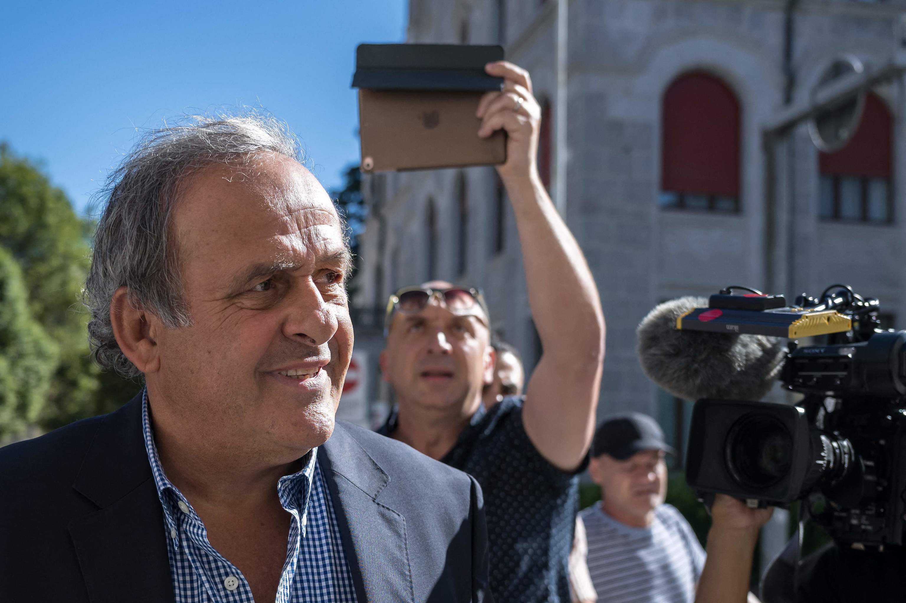 El ex presidente de la UEFA Michel Platini (izq.), rodeado de periodistas, mira mientras llega al Tribunal Penal Federal de Suiza para escuchar el veredicto de su juicio por un presunto pago fraudulento, en la ciudad de Bellinzona, al sur de Suiza, el 8 de julio de 2022
