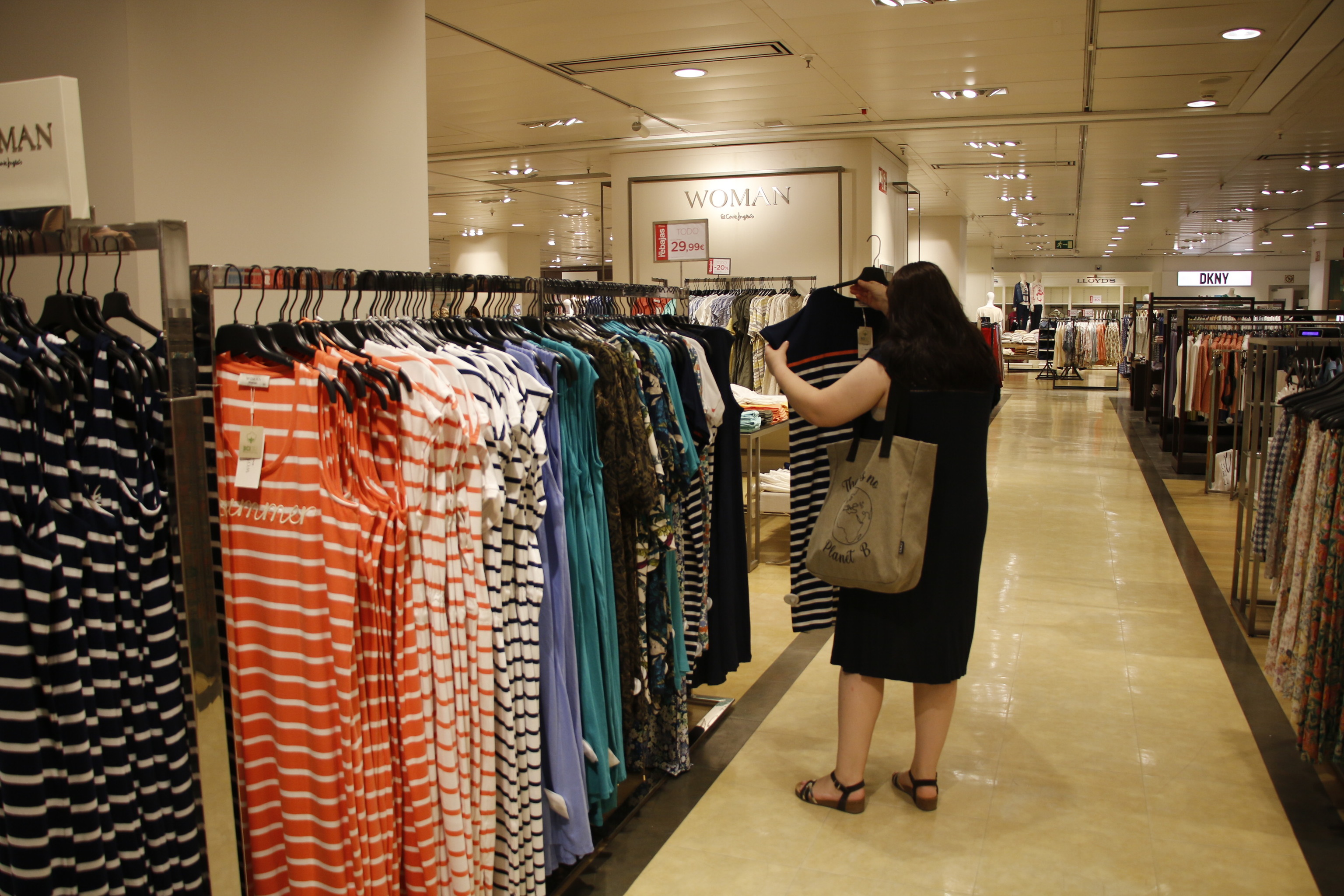 Una mujer mira prendas de ropa en un local comercial.
