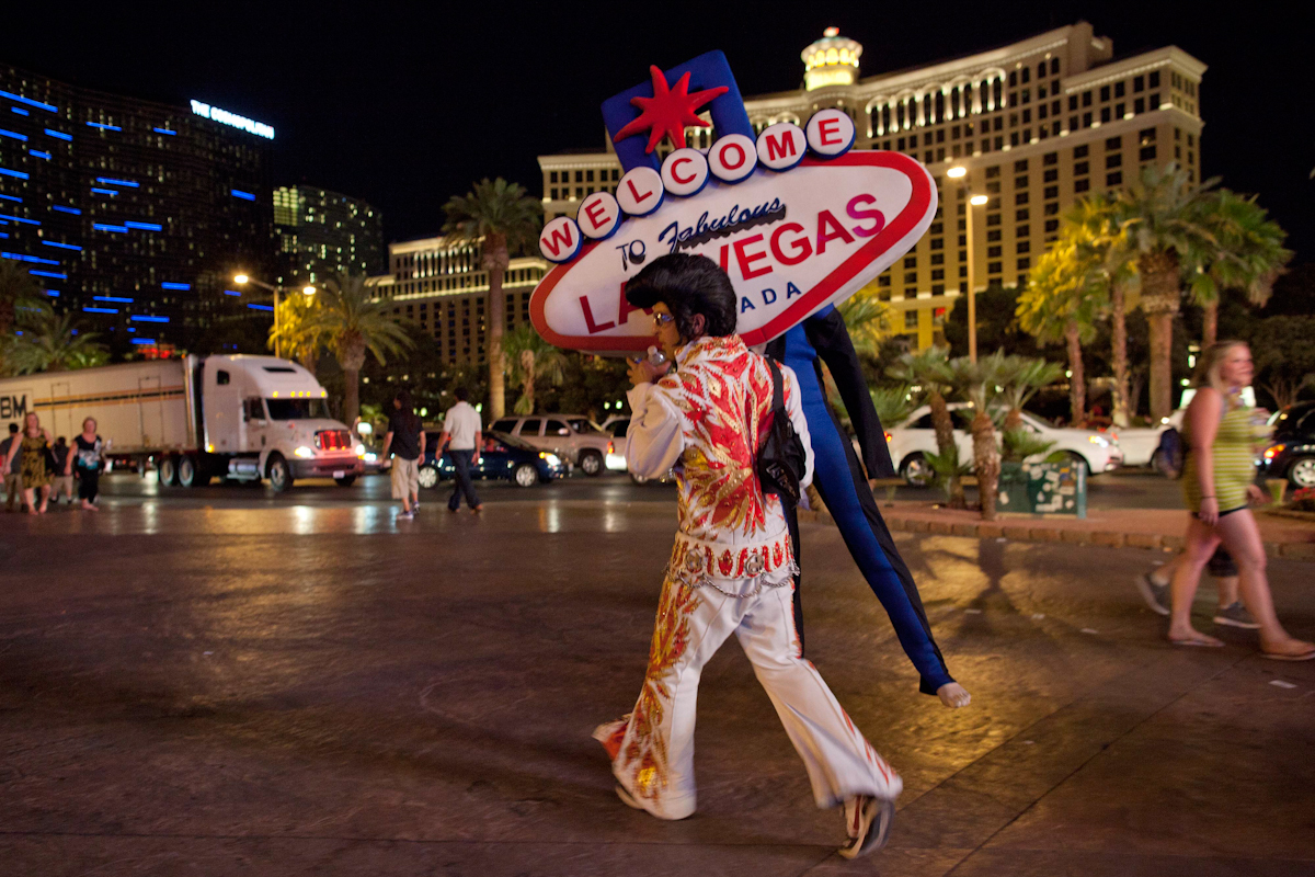Un hombrre vestido de Elvis cargaun cartel de Las Vegas