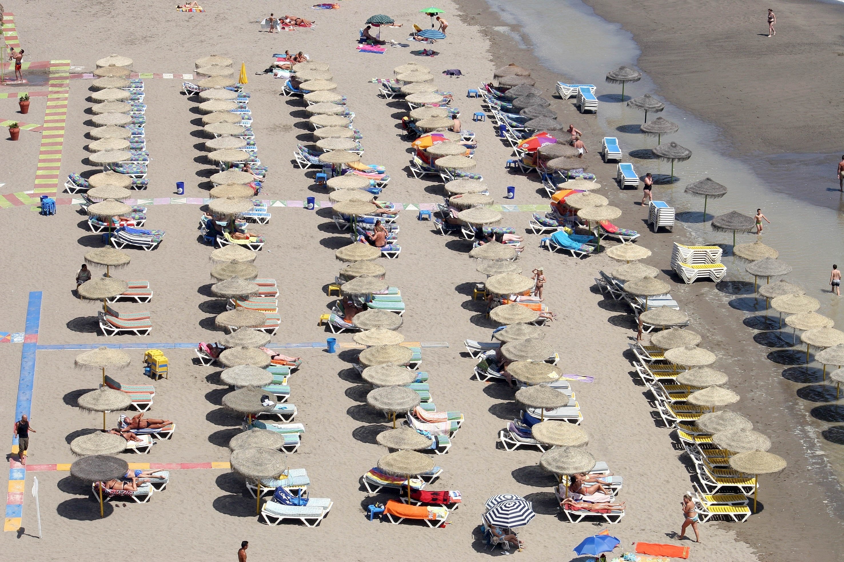 Vista aérea y panorámica de la playa de Torremolinos, en Málaga, con su arena cubierta por sombrillas y hamacas.