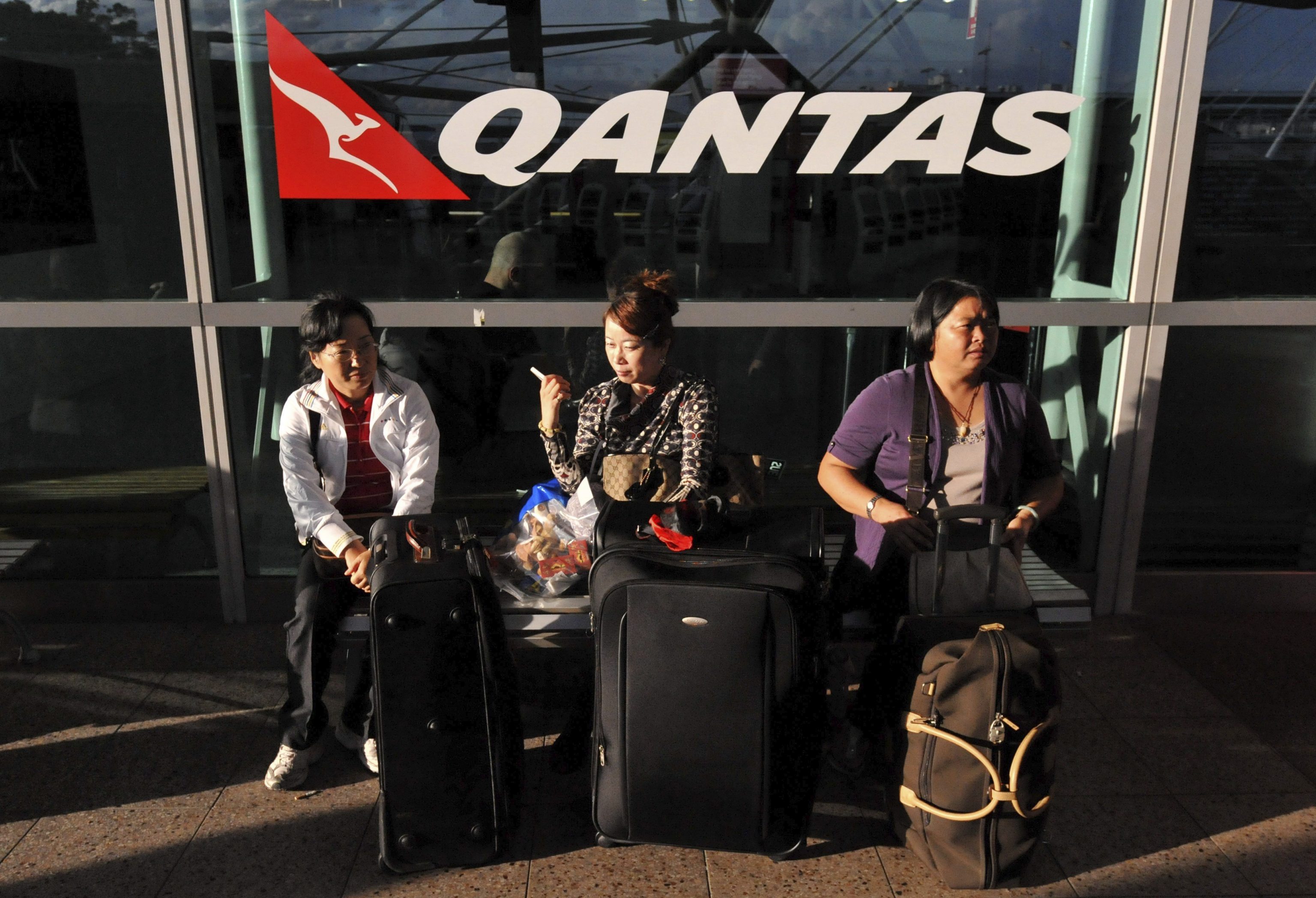 Pasajeros esperan con su equipaje con el logo de Qantas a sus espaldas
