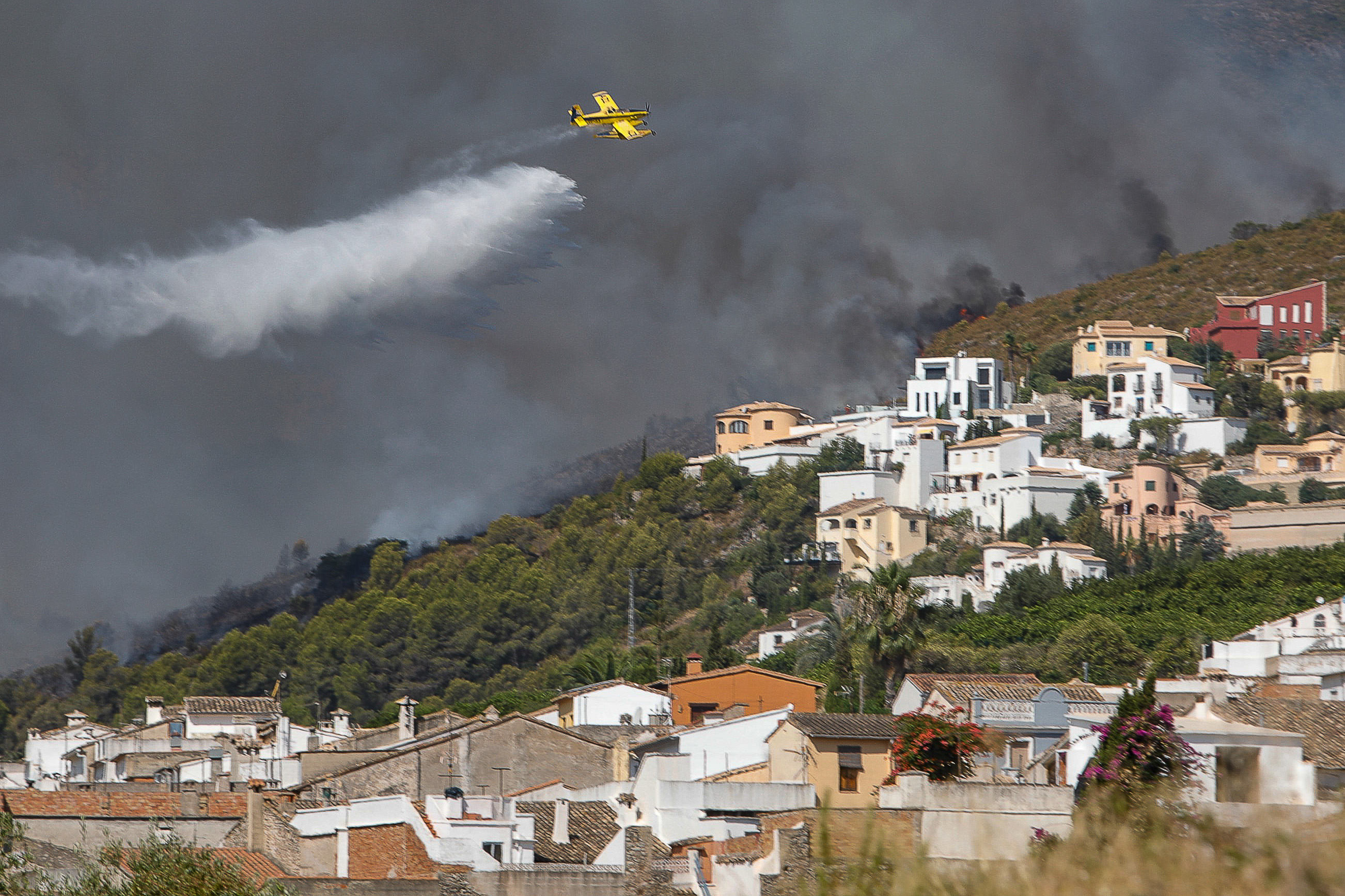 Una avioneta realiza una descarga de agua sobre las llamas que avanzan hacia una zona de viviendas en la Atzubia