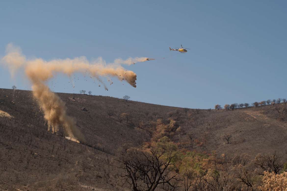 Un helicptero descarga bloques de paja sobre la superficie quemada en los incendios