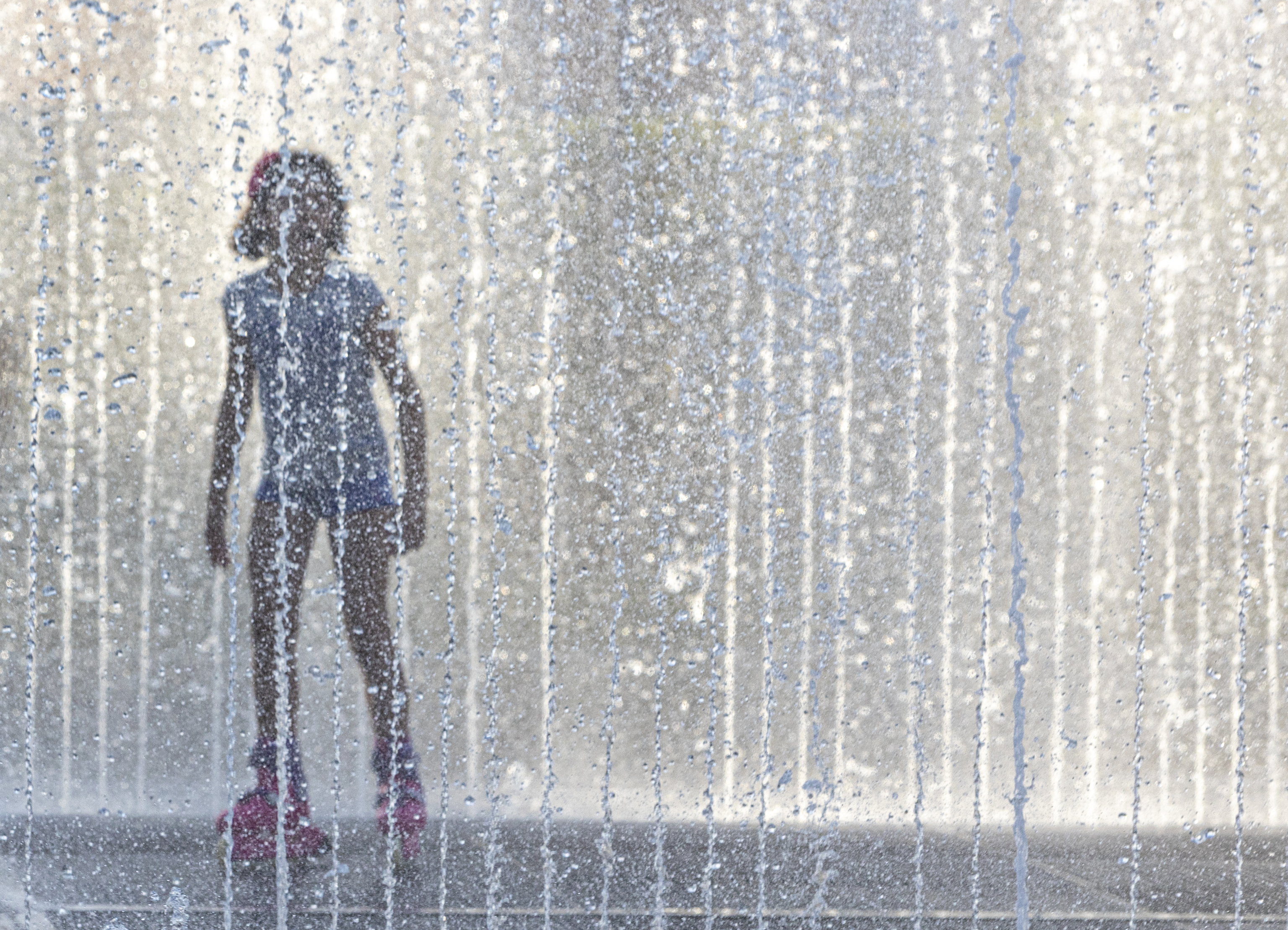 Un joven se refresca en una fuente durante una ola de calor.
