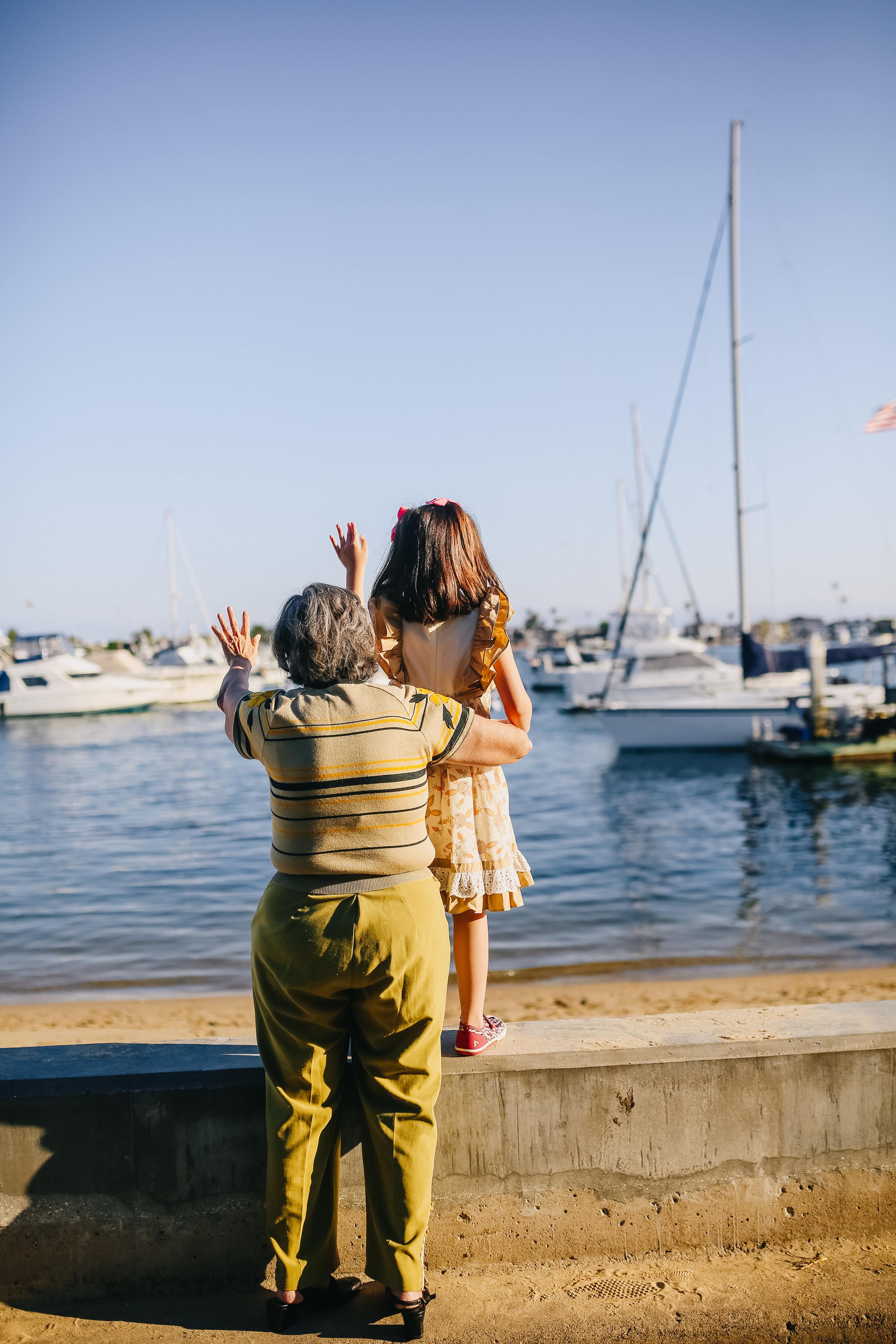 Una mujer y una nia hacen gestos de despedida en un puerto.