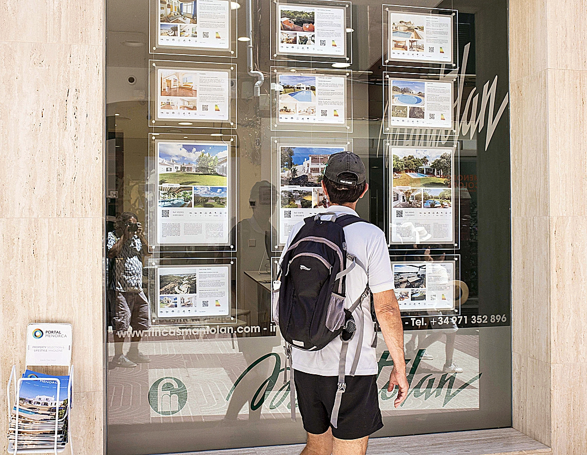 Un hombre observa carteles de viviendas en Menorca en venta.