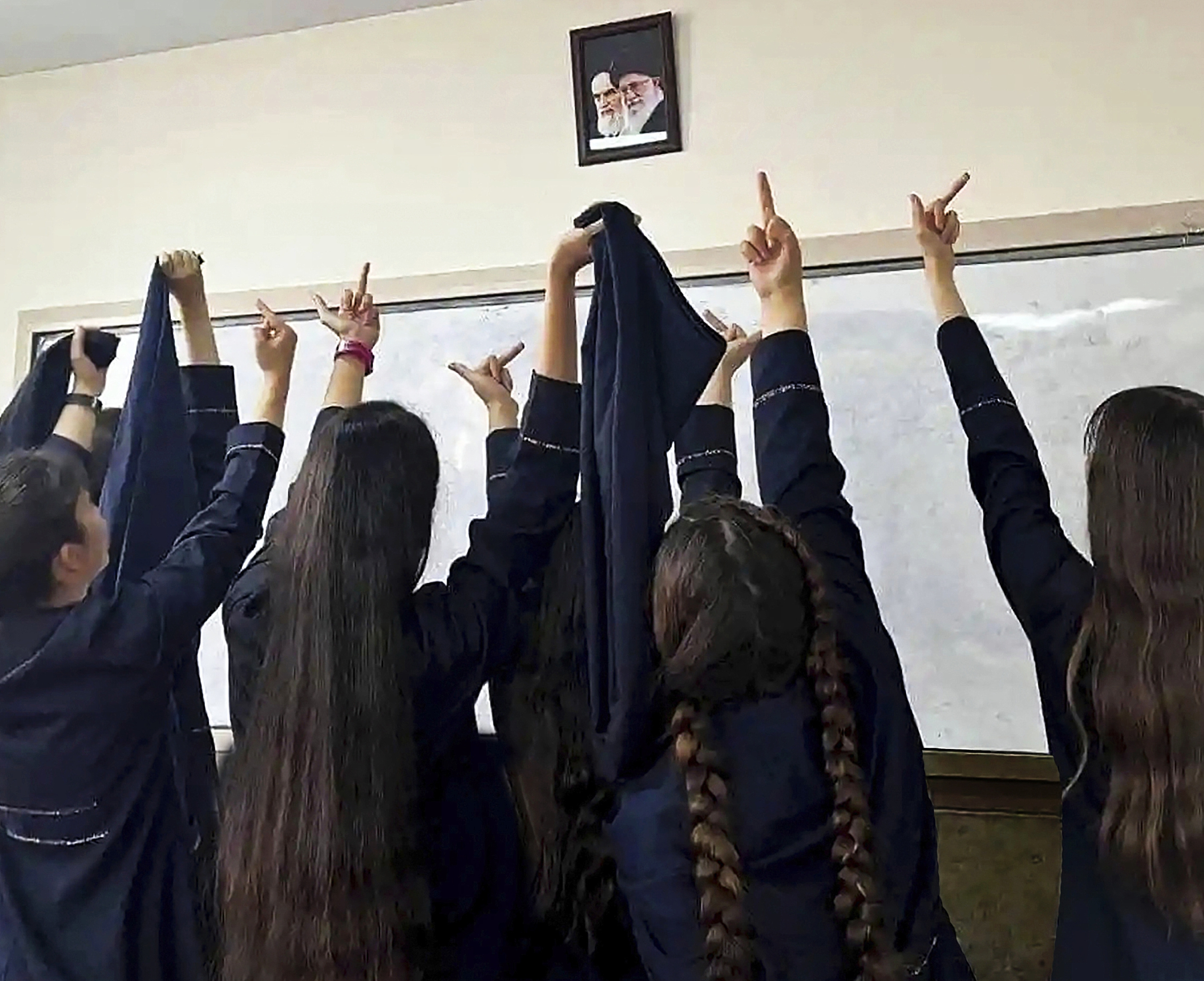 Alumnas de un instituto hacen una peineta a una foto del Ayatol Jomeini y del actual lder supremo, Ali Jamenei.