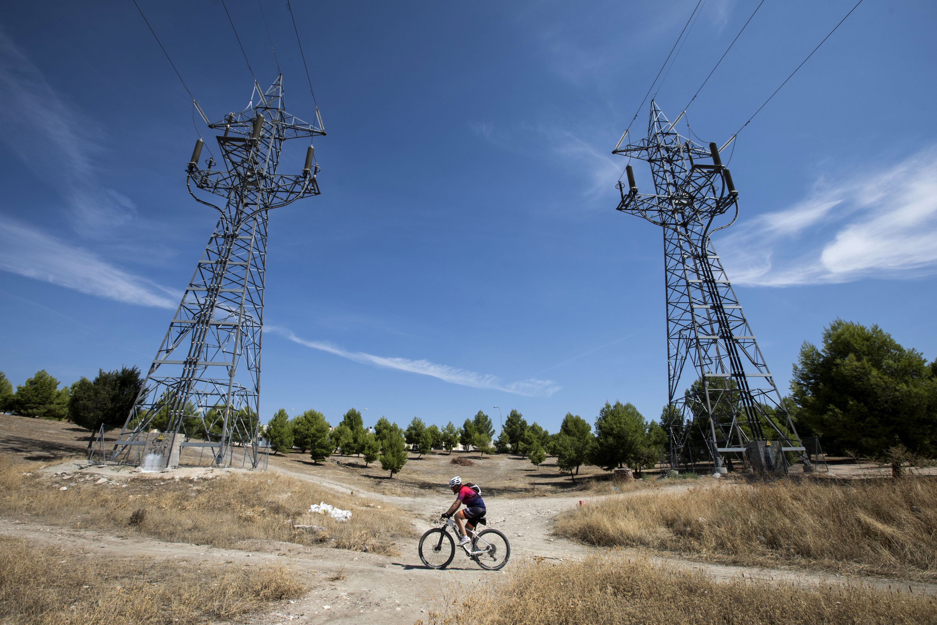 Un ciclista pasa ante dos torres de alta tensión en el Ensanche de Vallecas, Madrid.