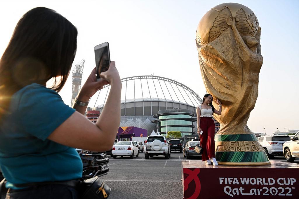 Una mujer posa frente a una réplica gigante del trofeo de la Copa del Mundo frente al estadio Khalifa de Doha.