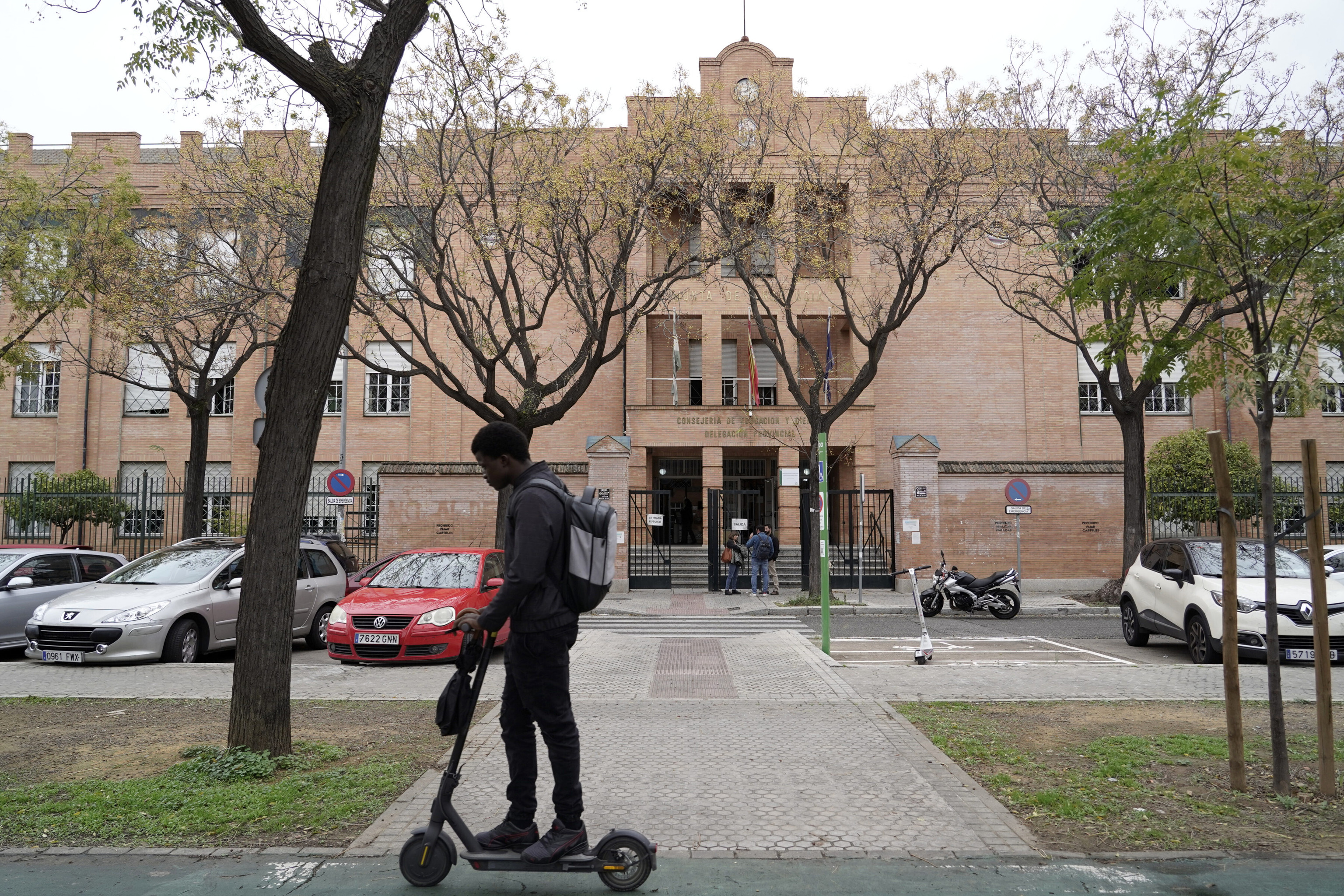 Un joven en patinete pasa ante las puertas de la Delegación de Educación de Sevilla.