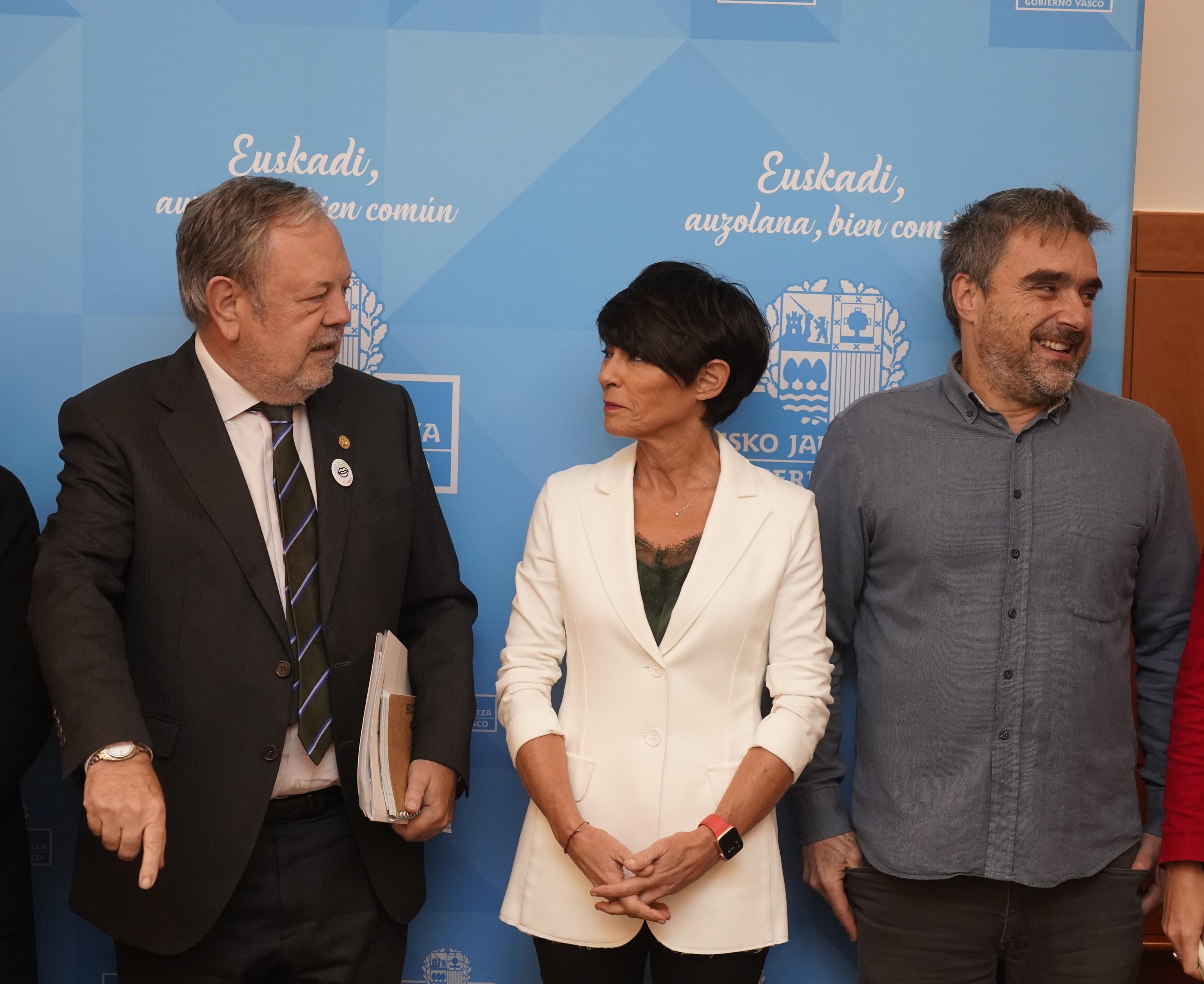 El consejero Azpiazu y la parlamentaria Maddalen Iriarte conversan ante un sonriente Mikel Otero en la sede del Gobierno vasco.