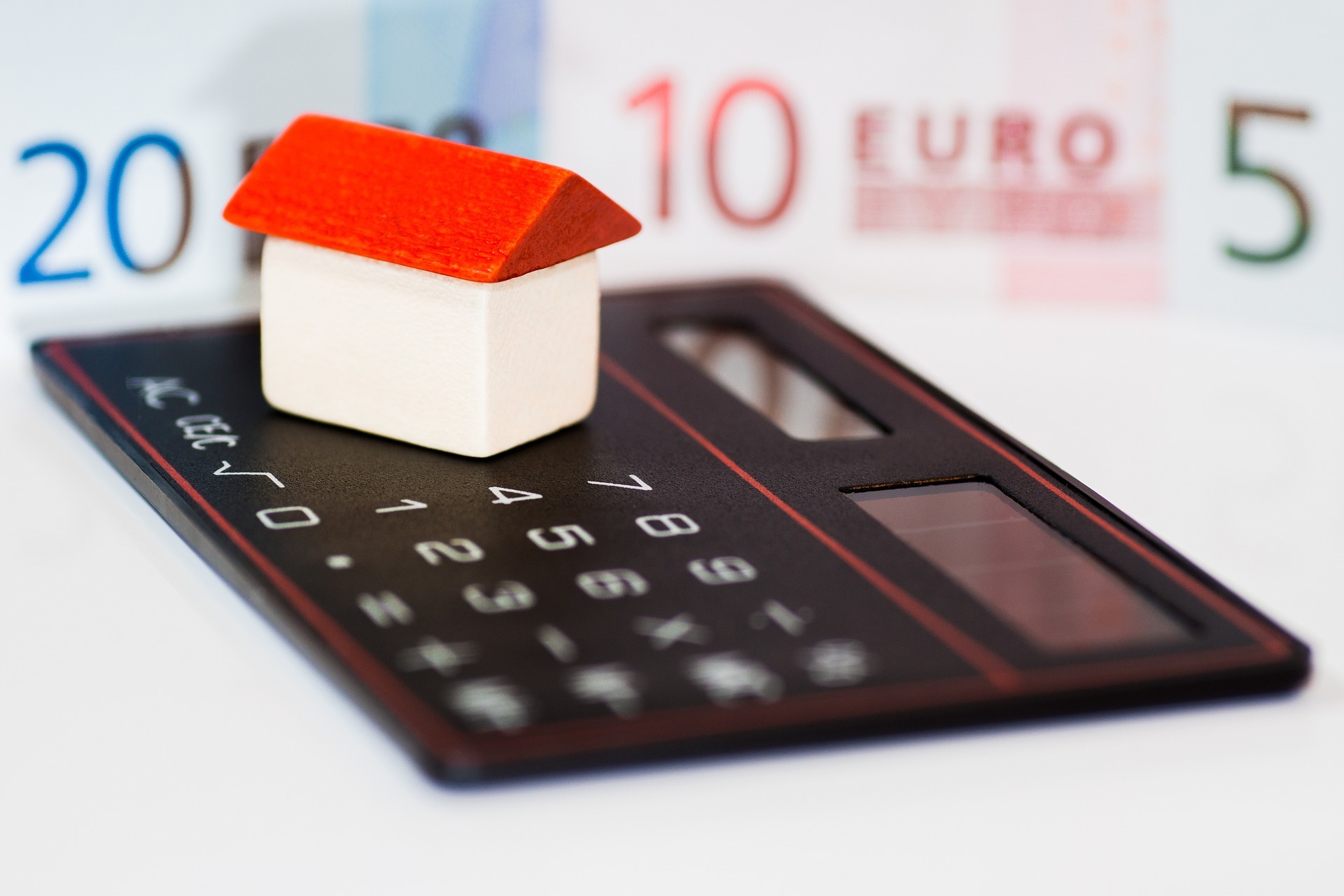 Una figura de una vivienda sobre una calculadora y frente a unos billetes.