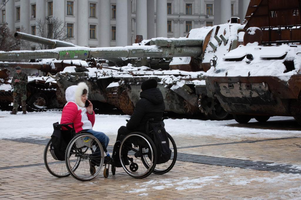 Mujeres en silla de ruedas hablan cerca de unos tanques rusos destruidos y expuestos en el centro de Kiev.