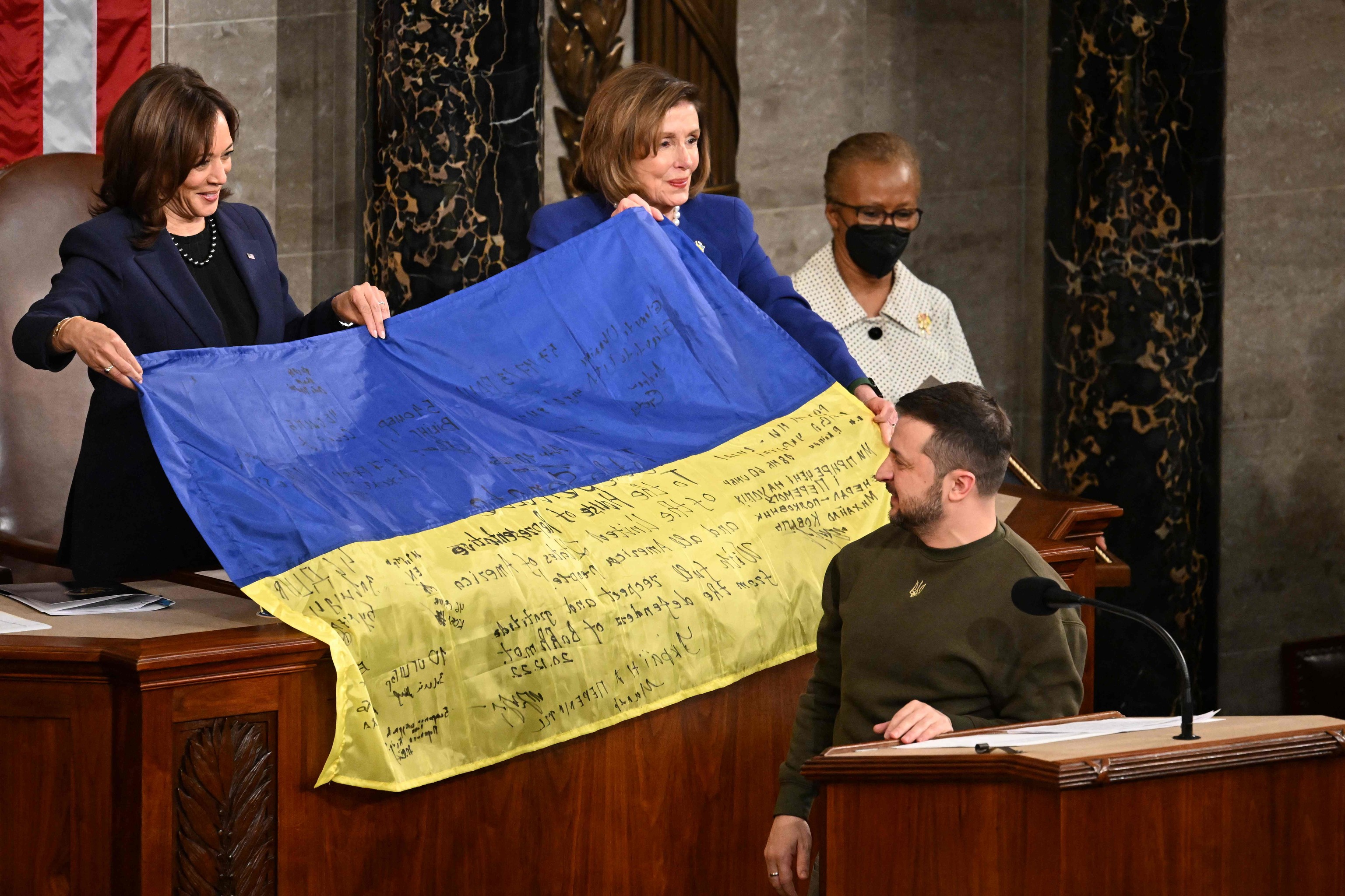 Zelensky hands over a flag signed by soldiers to Nancy Pelosi.