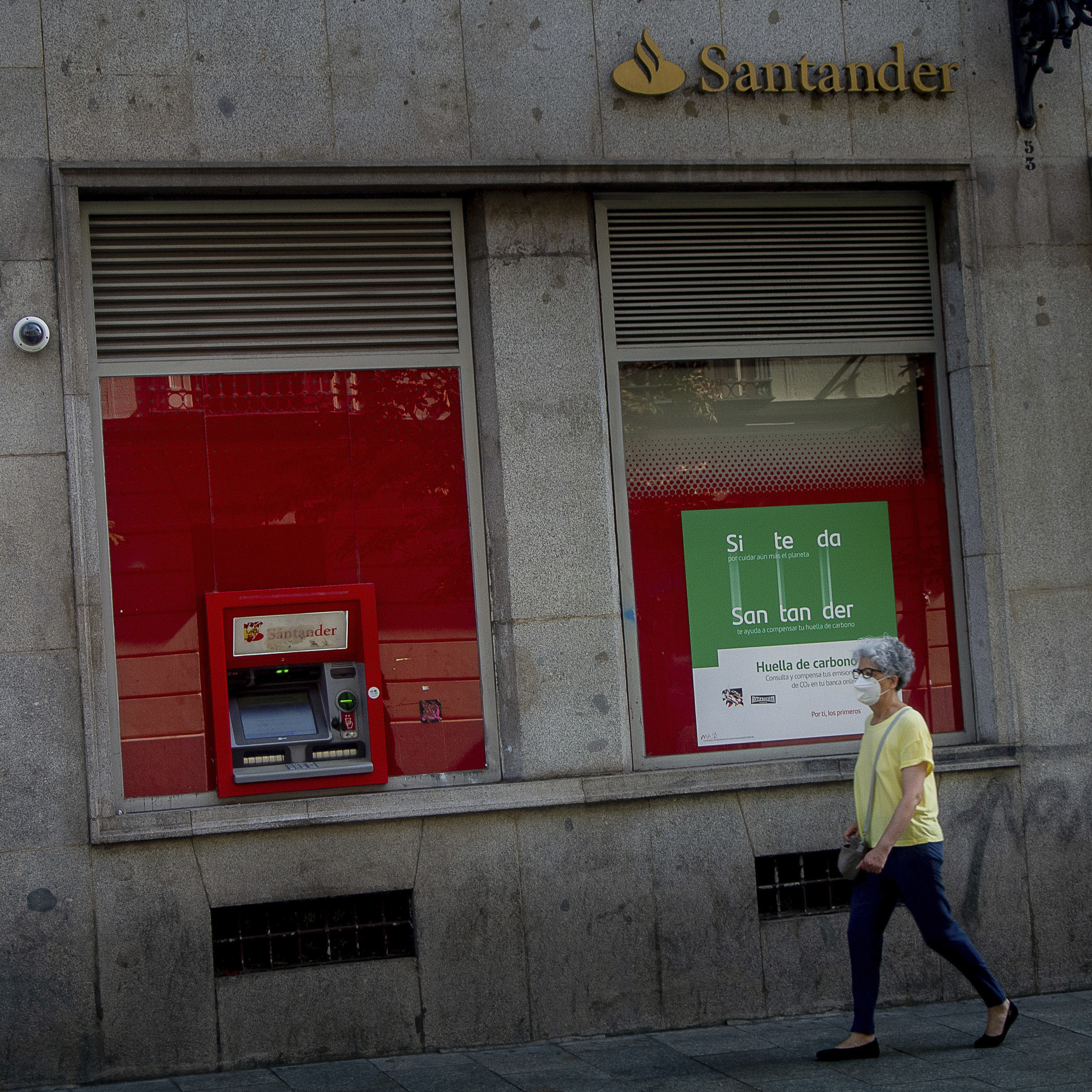Una mujer andando por delante de la fachada de una sucursal del Banco Santander.