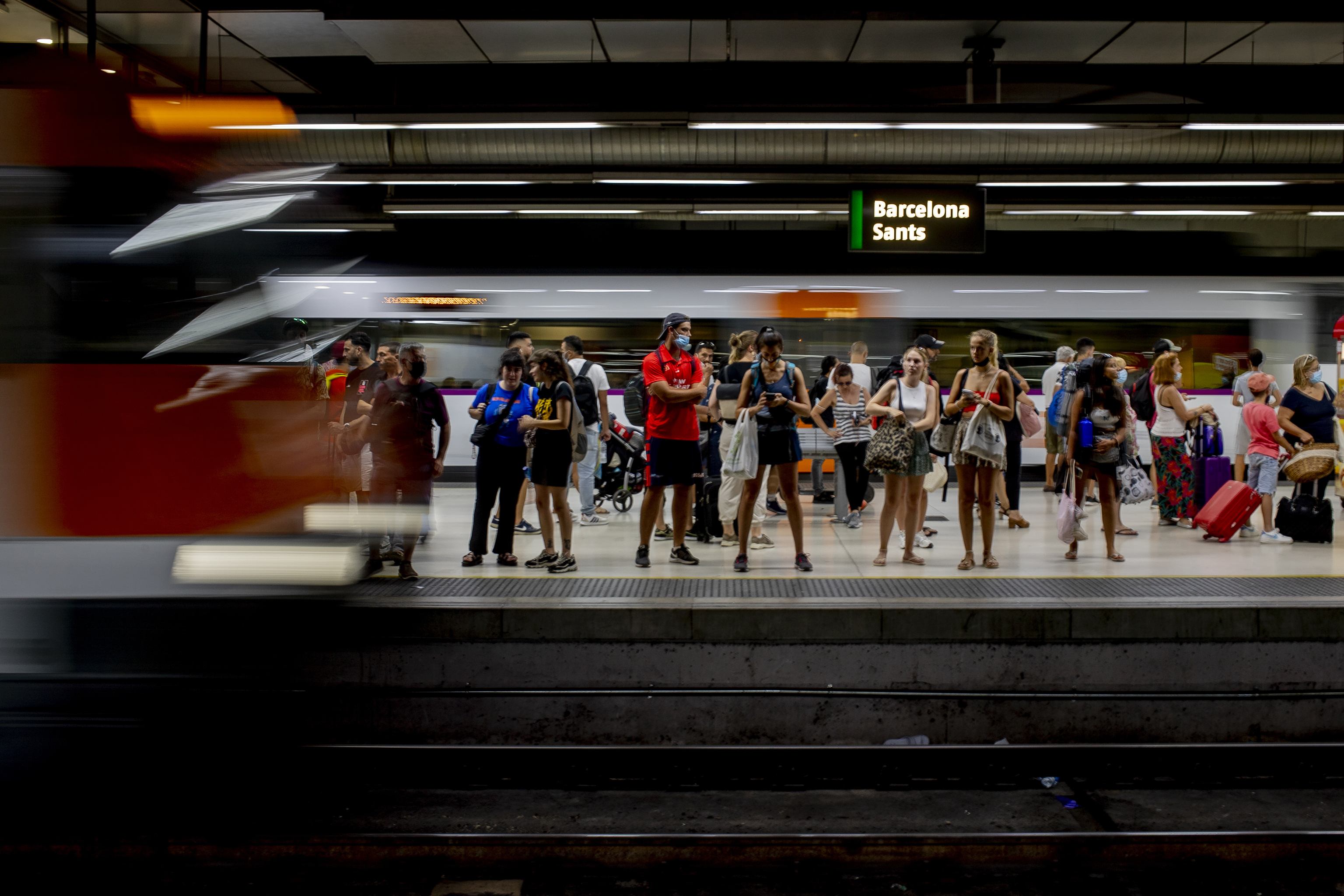 Un grupo muy numeroso de usuarios espera al tren mientras por otra via circula un tren de Rodalies.