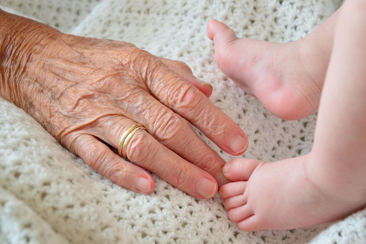 Bisnieto o biznieto. Imagen de una mano anciana junto a los pies de un beb