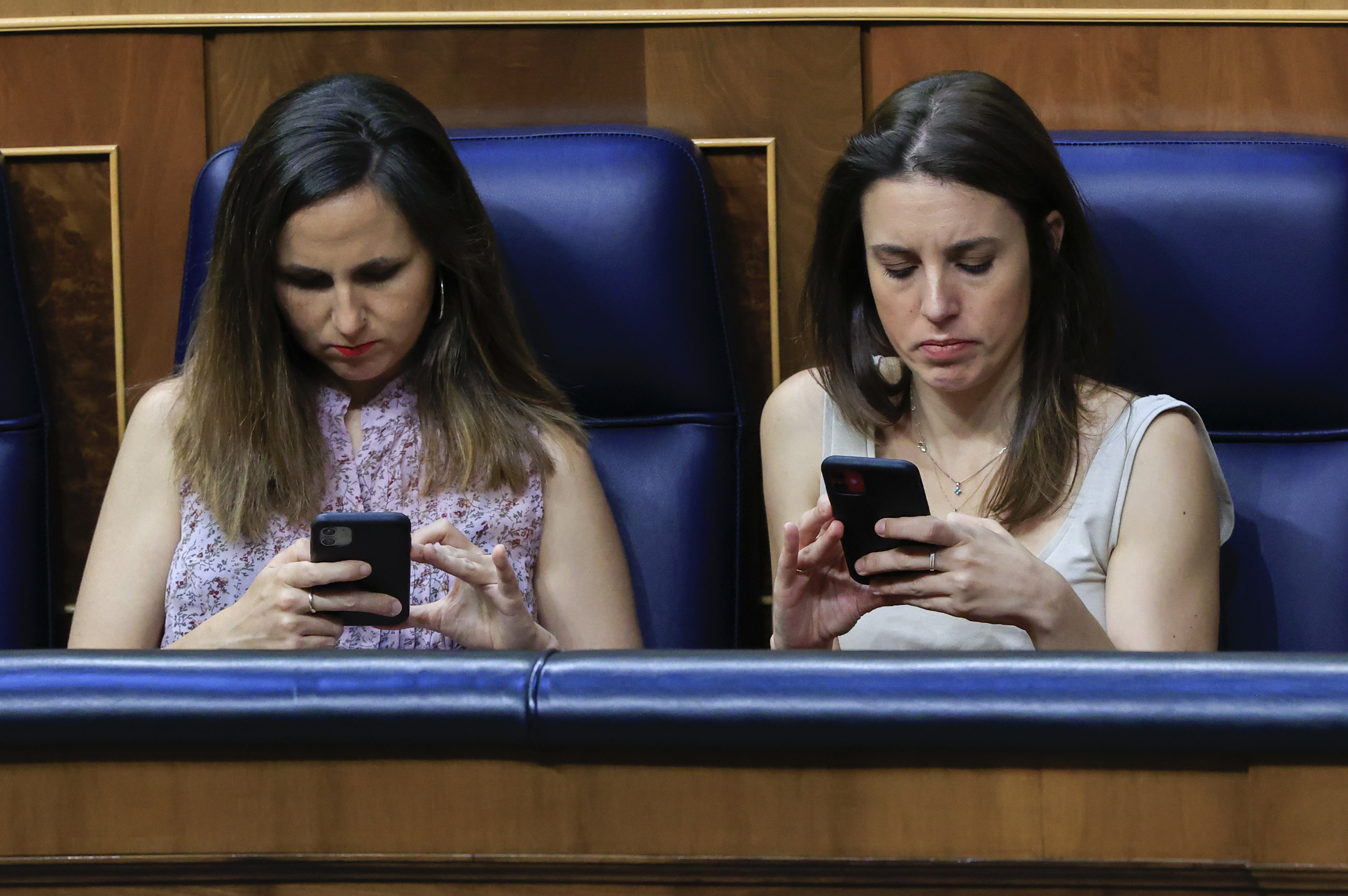 Irene Montero y Ione Belarra miran sus móviles en el Congreso.
