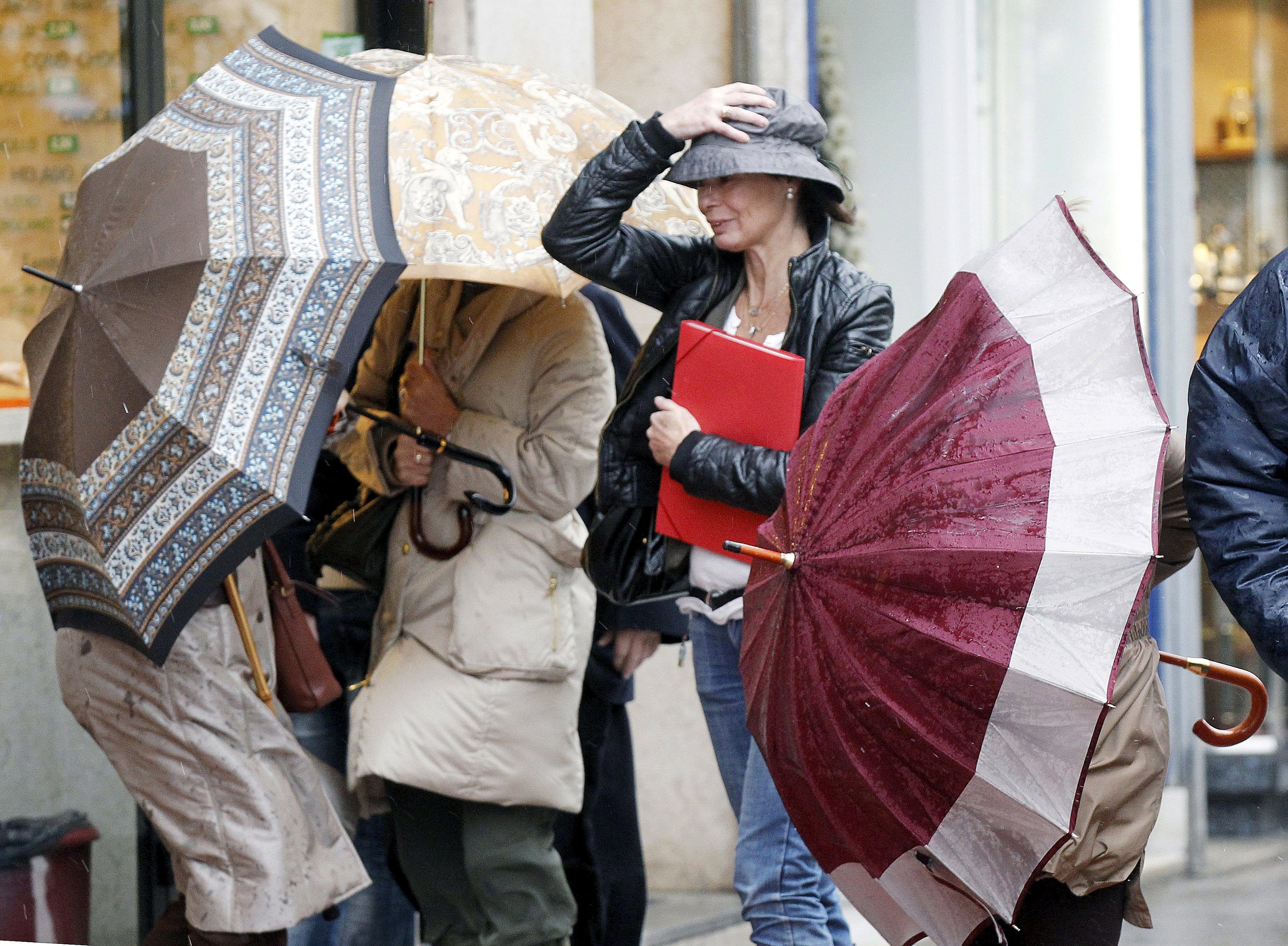 Varias personas intentando protegerse con el paraguas del fuerte viento en Santander.