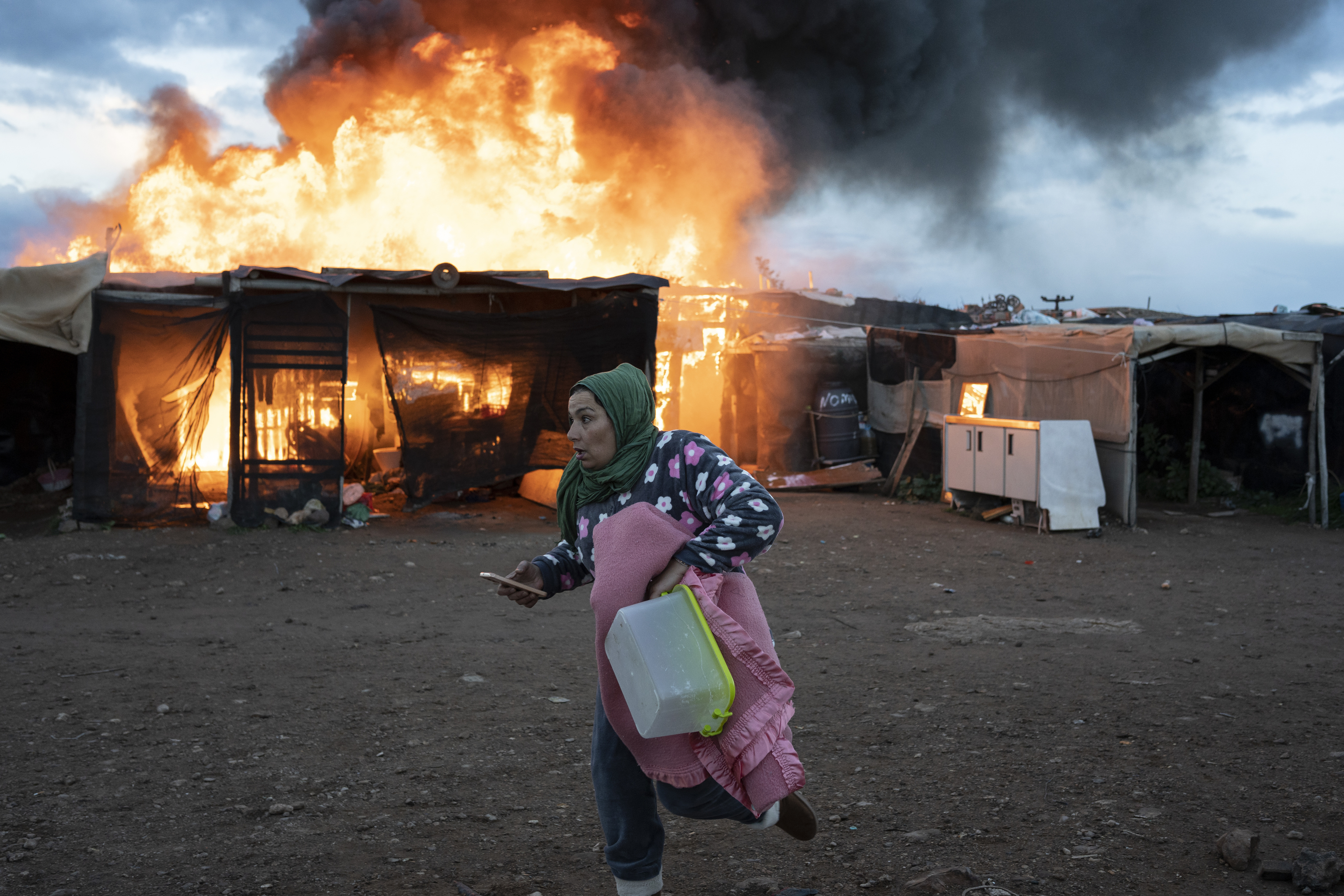 Una mujer sale corriendo mientras arde una de las chabolas del asentamiento de Njar.