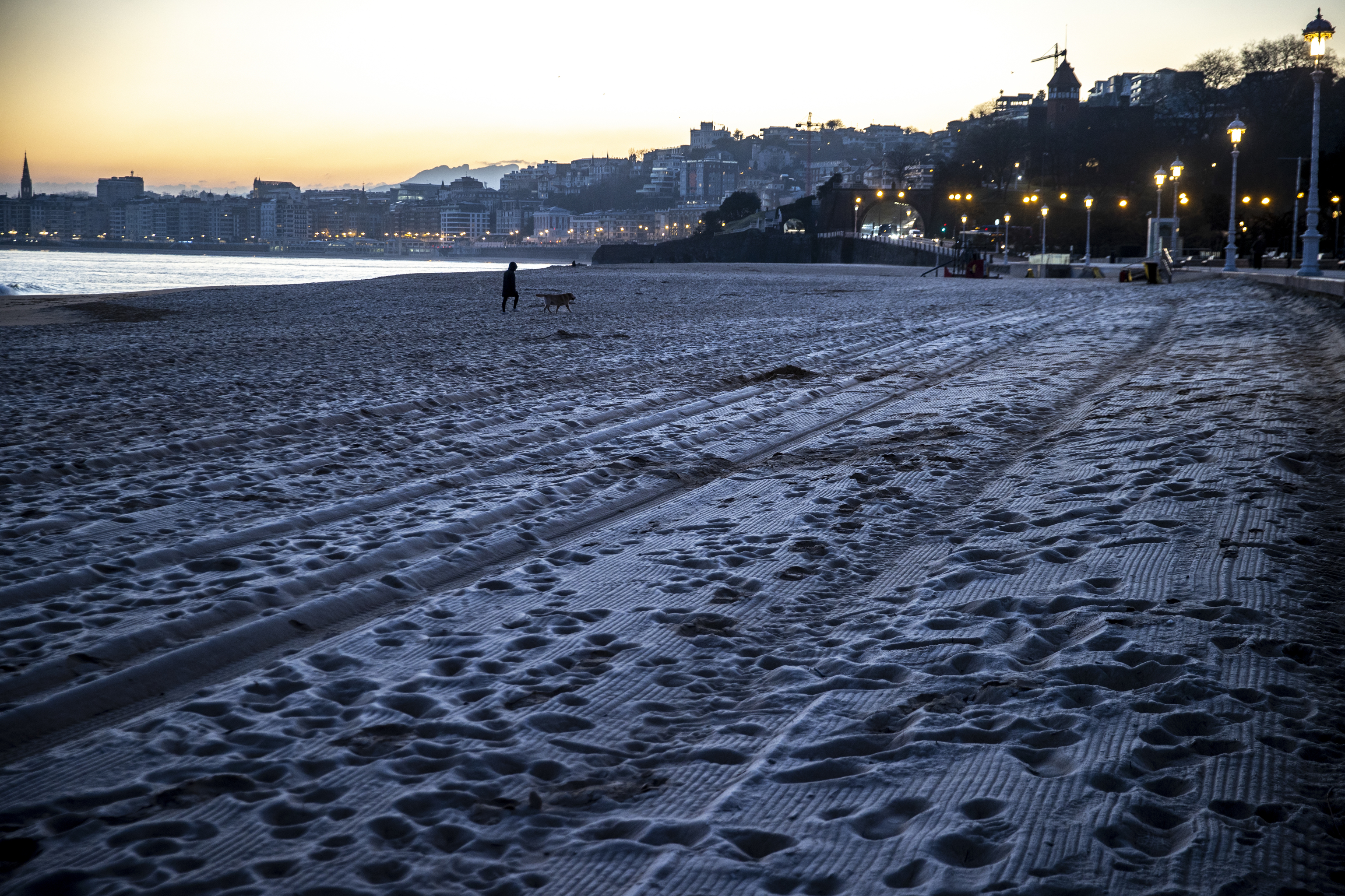 Una mujer pasea a su perro  por la playa de Ondarreta de San Sebastin, cuya arena ha amanecido helada.
