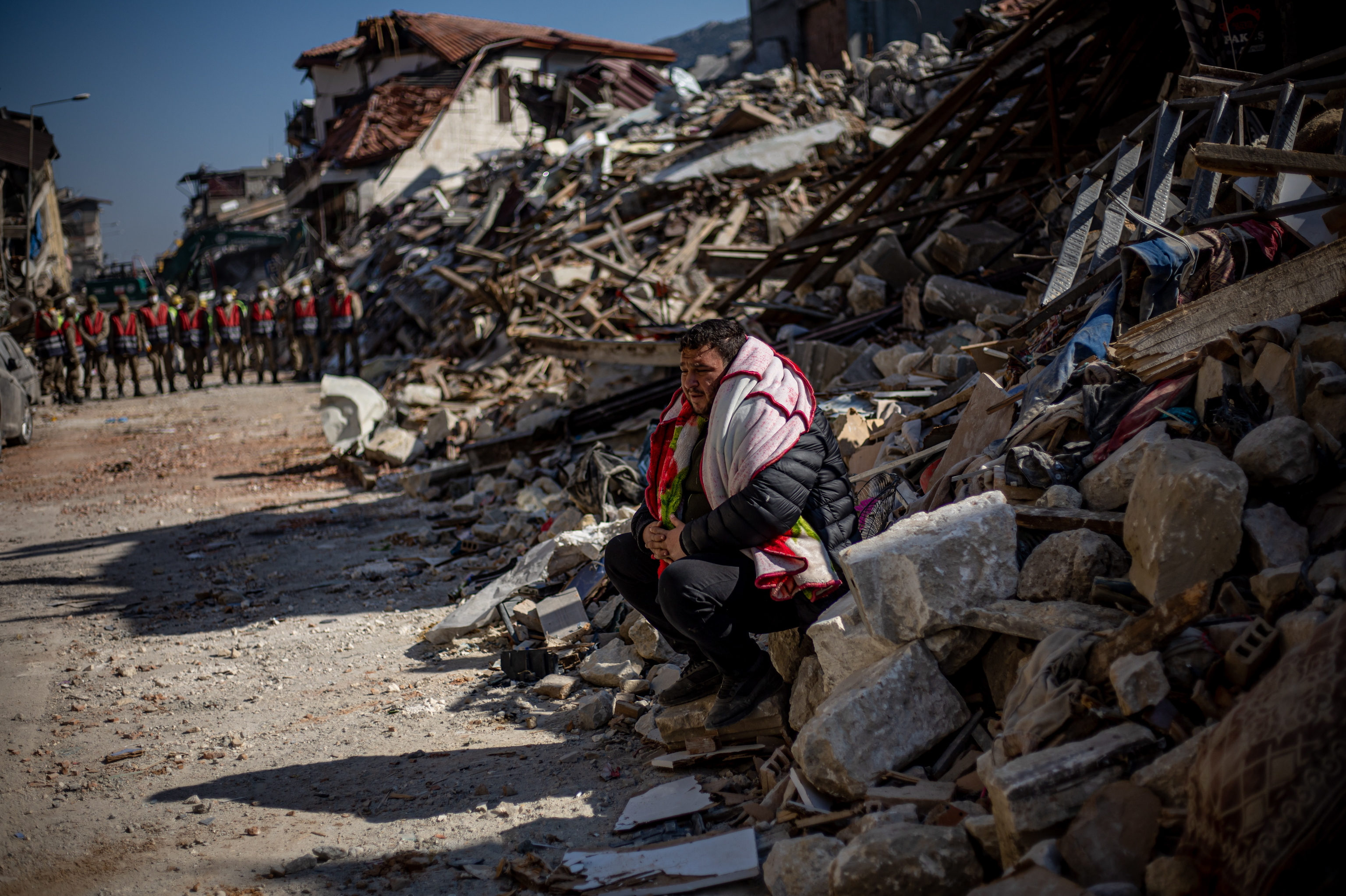 Un hombre sentado sobre los escombros de edificios derrumbados en Hatay.