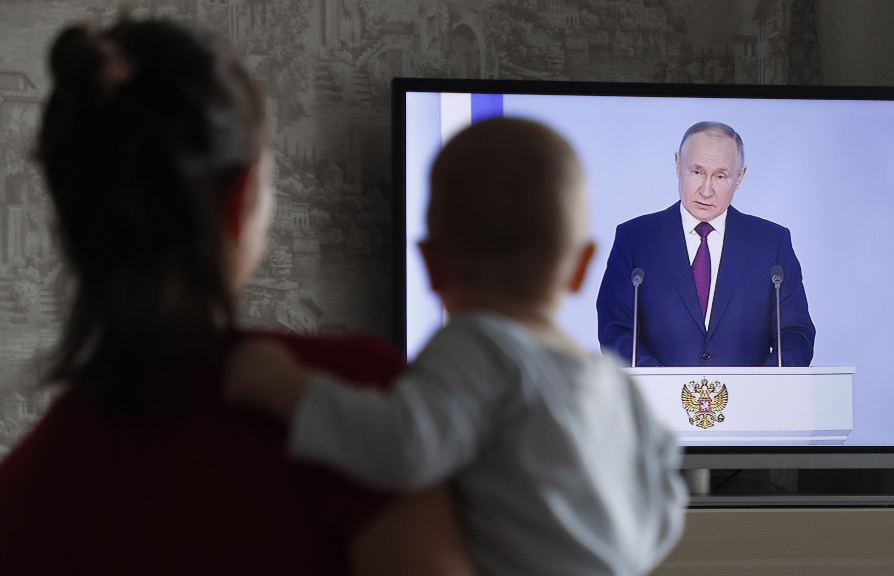 Una mujer sostiene a su hijo mientras ve el discurso de Putin por televisi