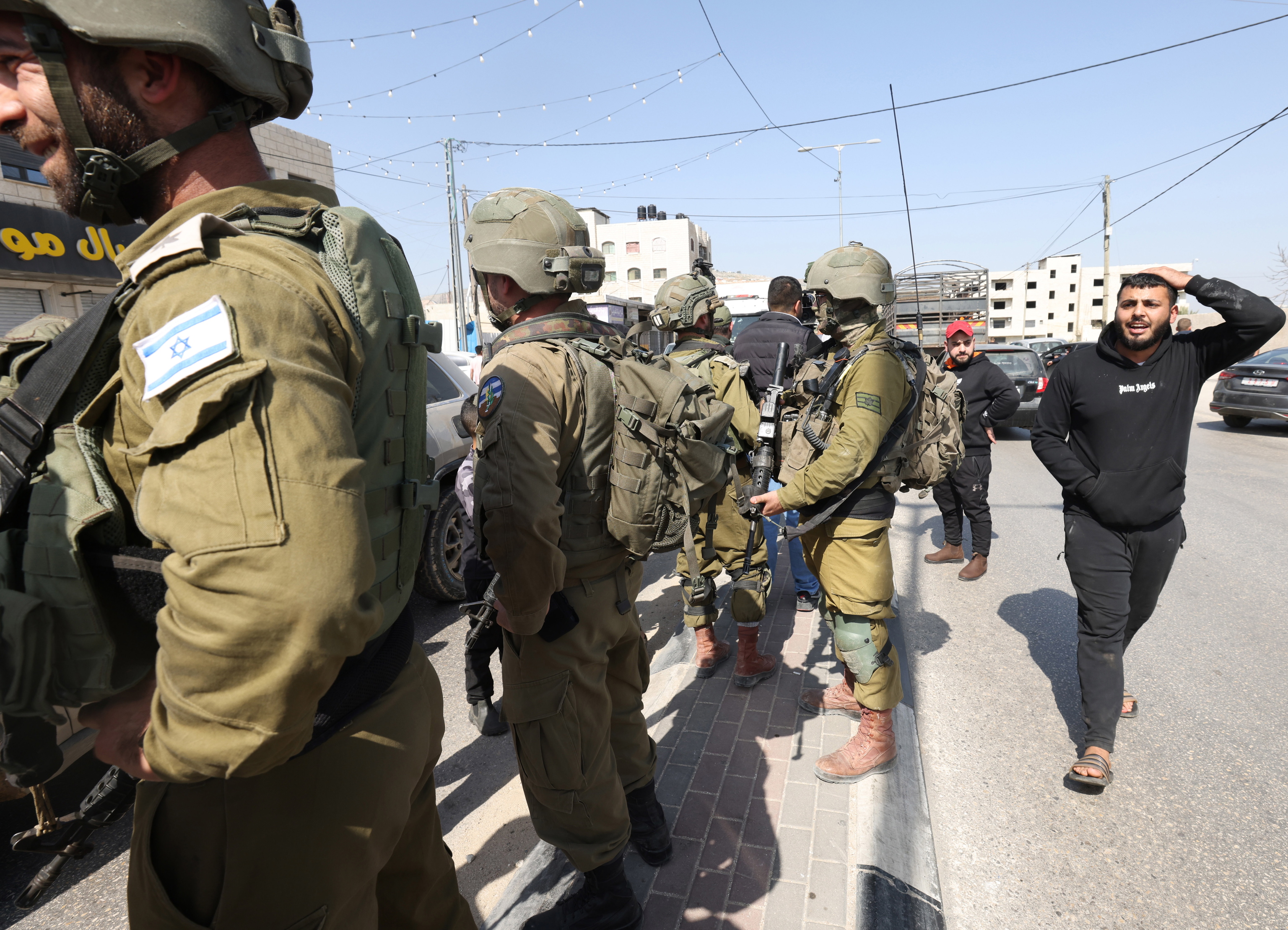 Un palestino pasa junto a un grupo de soldados israeles armados en Hawara.