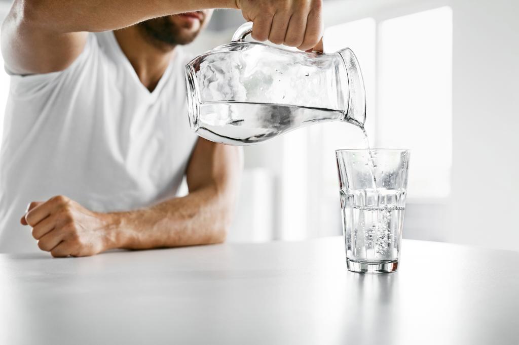 Hombre sirviéndose agua de una jarra a un baso de cristal.