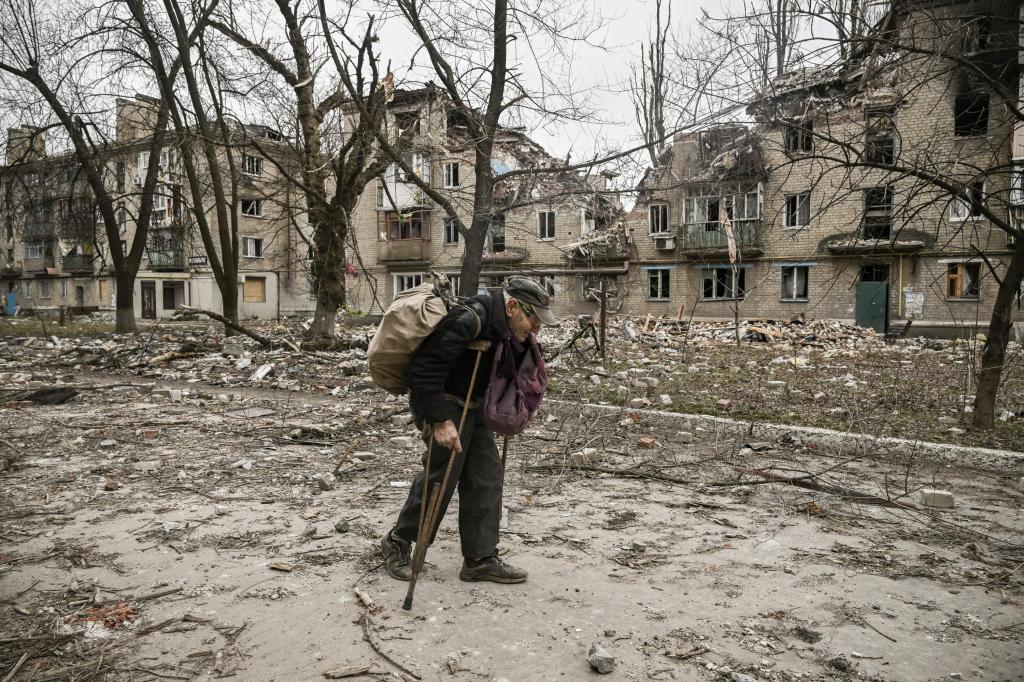 Un anciano recoge leña entre los escombros frente a un edificio destruido tras un ataque en la ciudad de Avdiivka, en Donetsk.