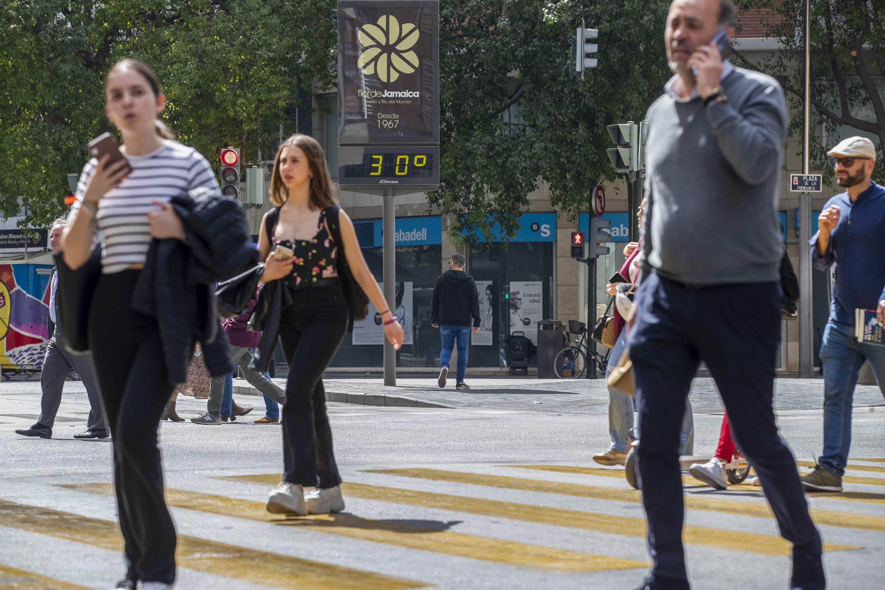 Varias personas cruzan un paso de peatones junto a un termmetro que marca 30 grados, este viernes en la Gran Va de Murcia.