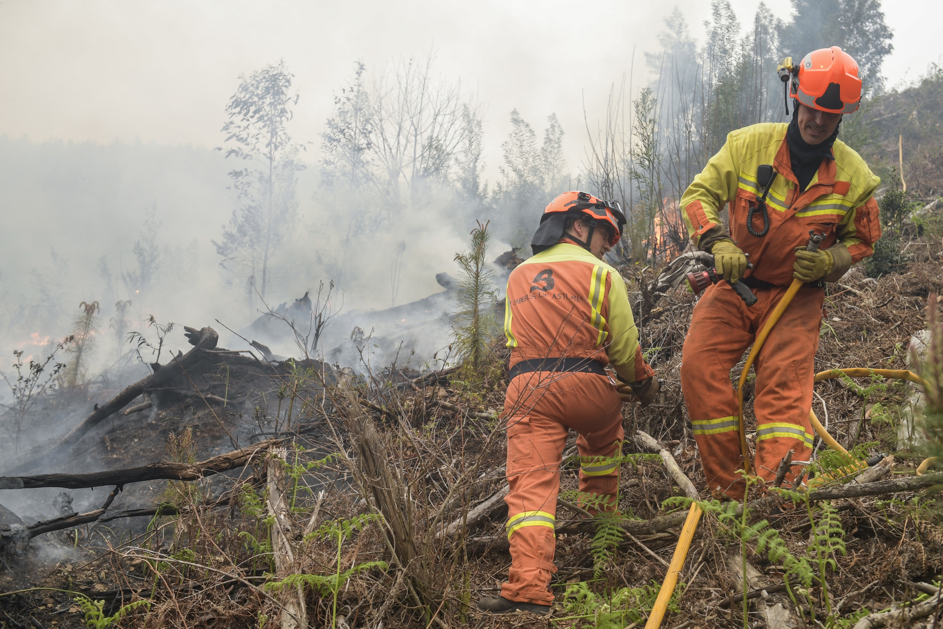 Dos miembros de los equipos de extinción trabajan para frenar el fuego en el municipio de Navelgas.