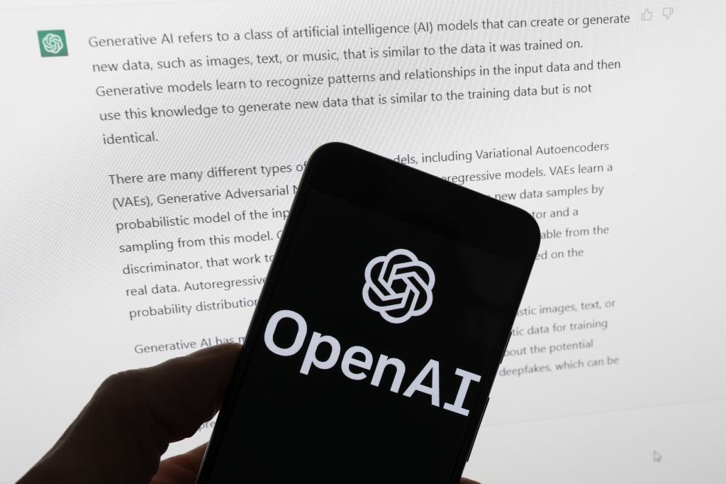 El logotipo de OpenAI en un teléfono móvil frente a una pantalla del ordenador que muestra ChatGPT