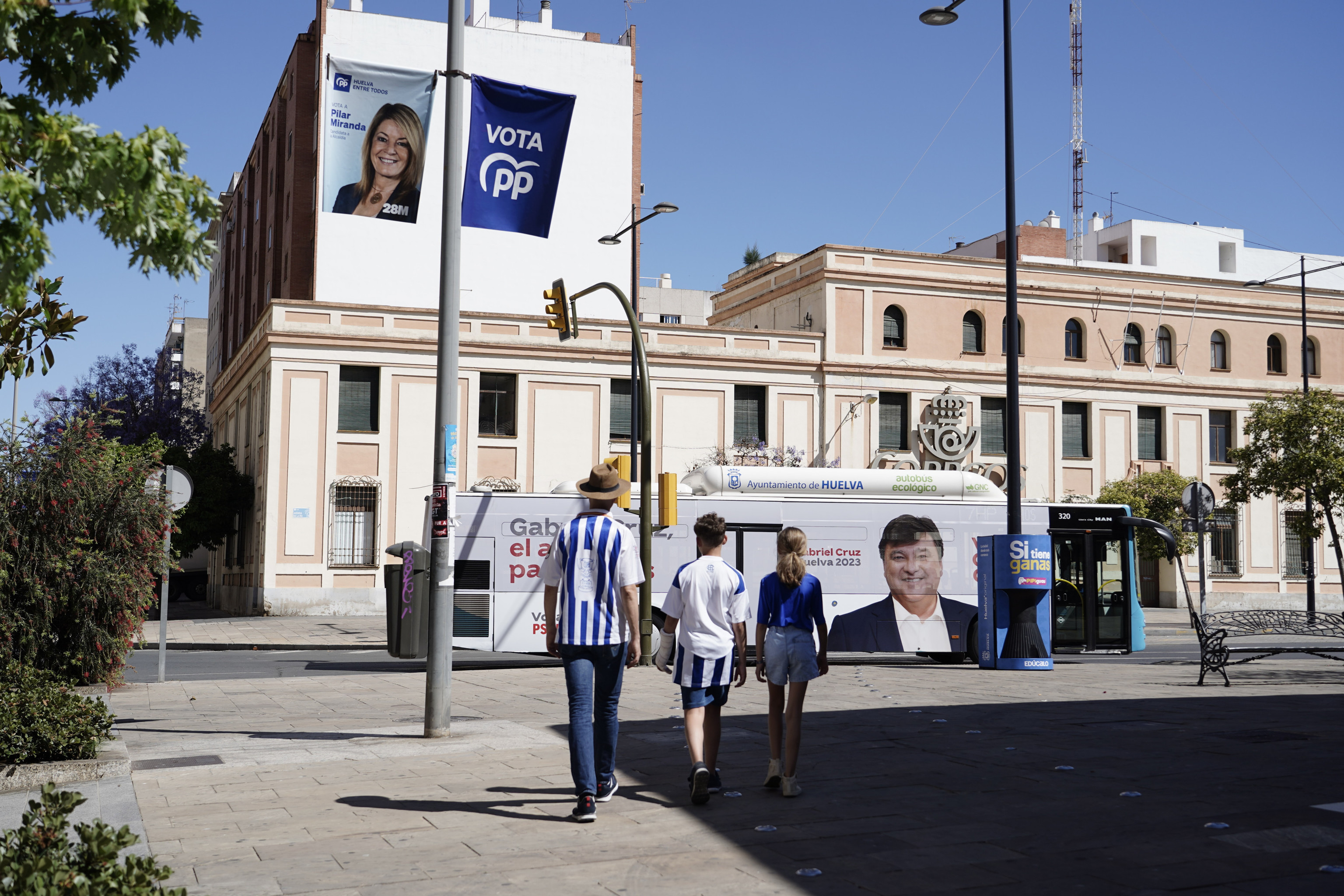 Tres seguidores del Recre, ante un autobs con el candidato del PSOE y banderolas con la 'nmero 1' del PP en Huelva.