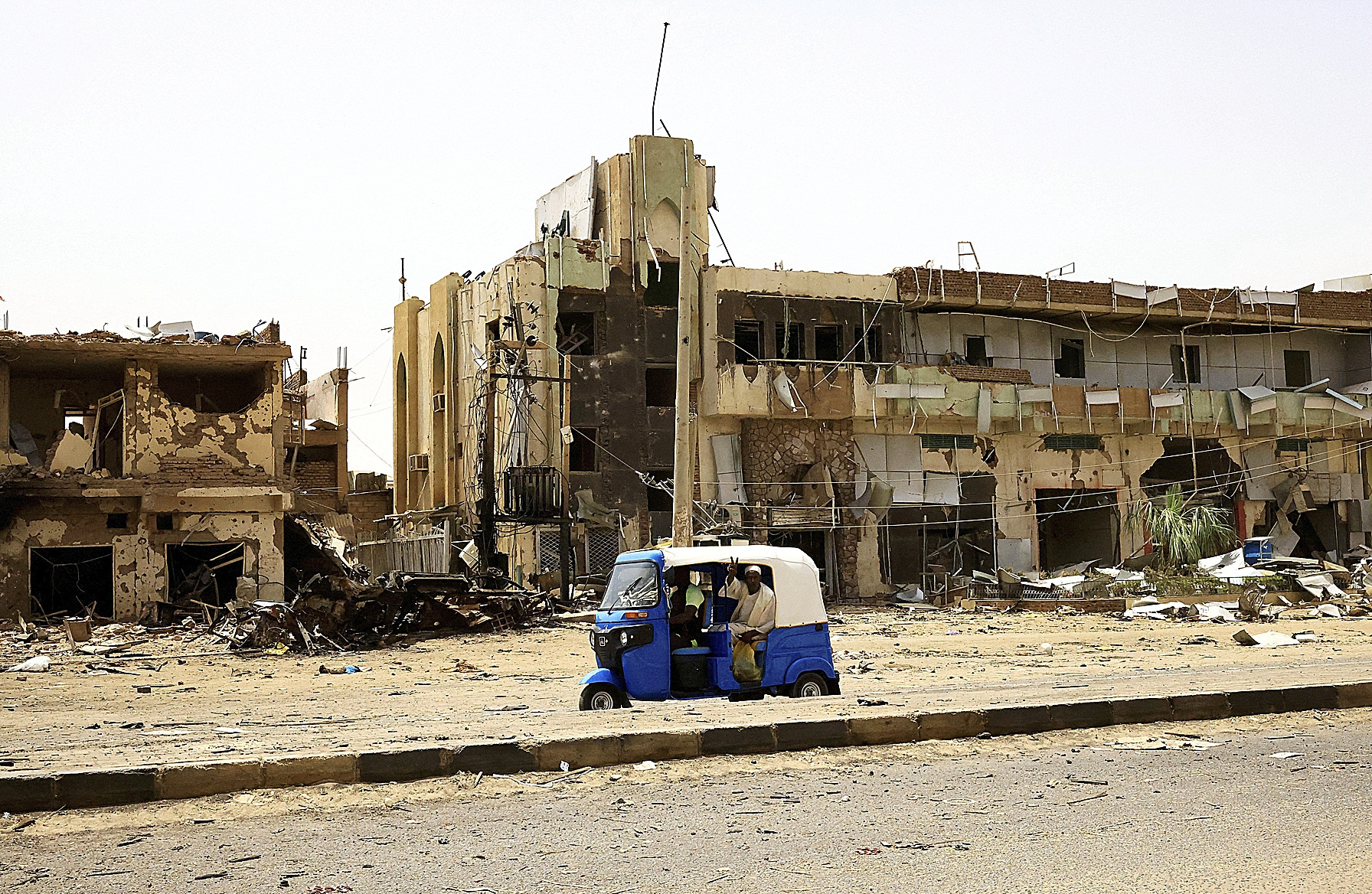 Civiles pasan en un vehículo junto a edificios dañados por los combates, en Jartum.