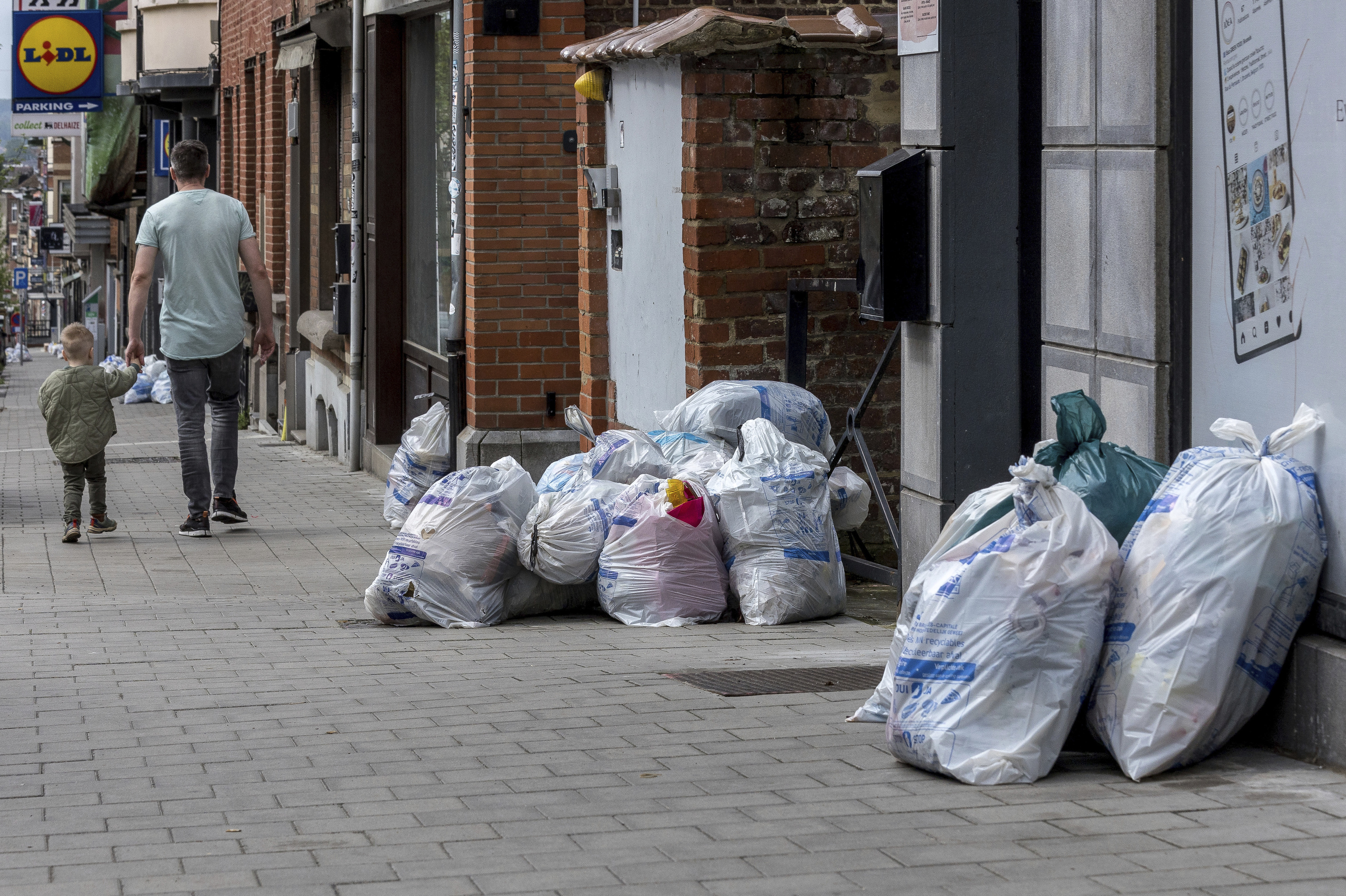 Un padre y su hijo caminan por una calle llena de basura en Bruselas.