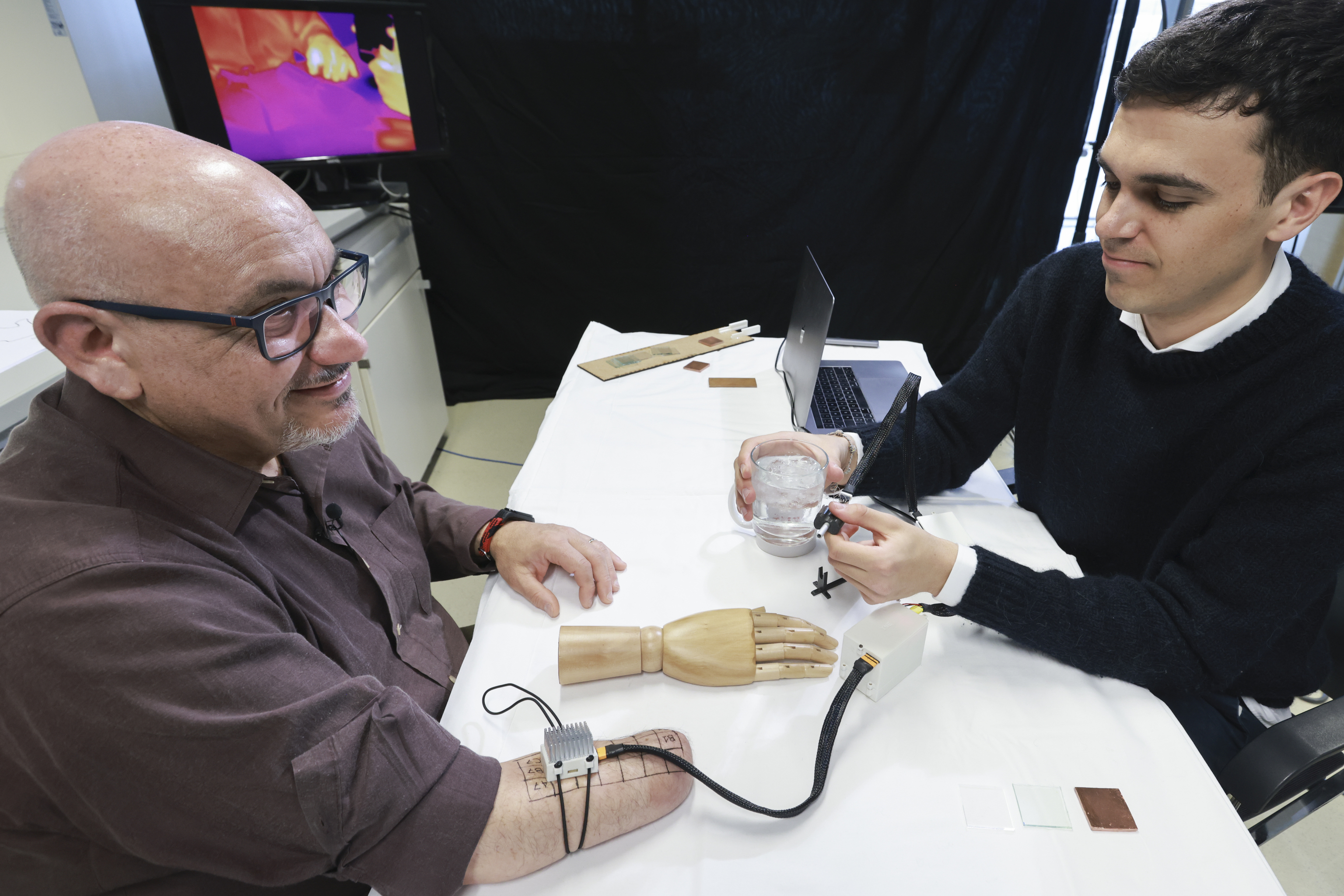El amputado Fabrizio Fidati (izquierda) experimenta la sensación térmica fantasma obtenida con el dispositivo MiniTouch, con el investigador y autor, Jonathan Muheim.