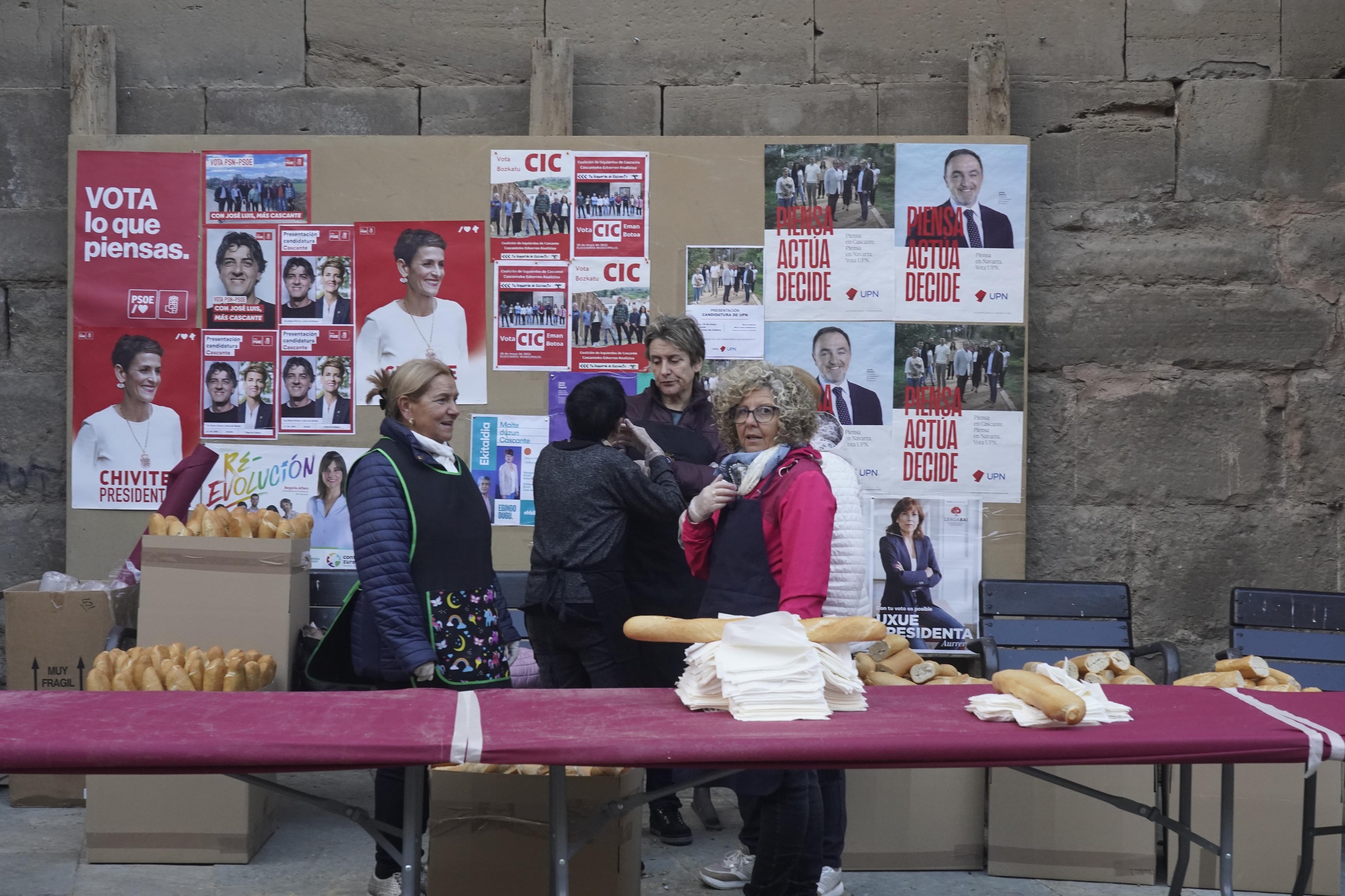 Vecinas se preparan junto a un cartel electoral para repartir bocadillos de chistorra en las fiestas de  Cascante.