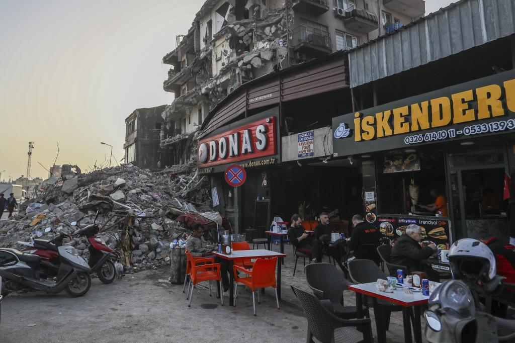 Varias personas, en una terraza junto a una zona destruida por los seísmos en Iskenderun.