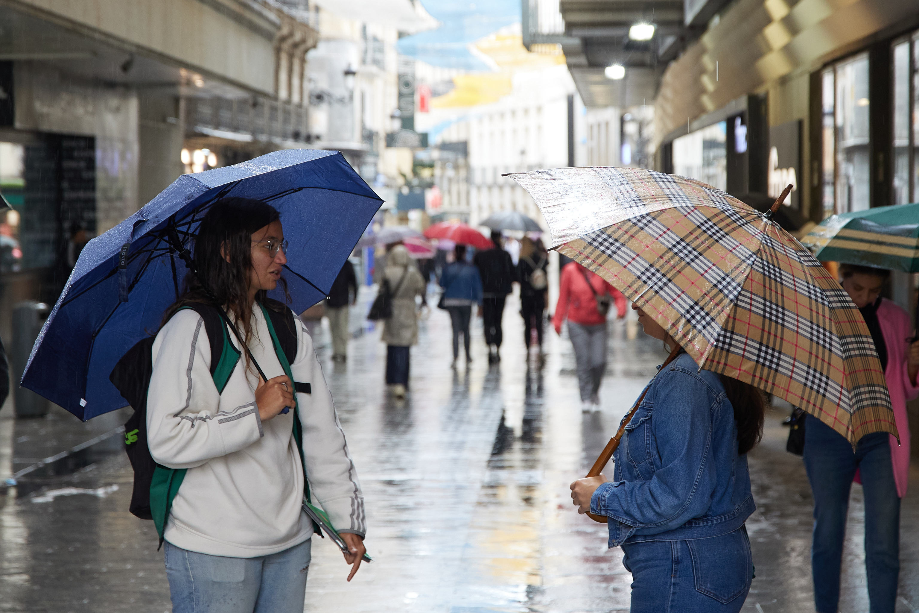Dos personas con paraguas caminando por una calle de Madrid.