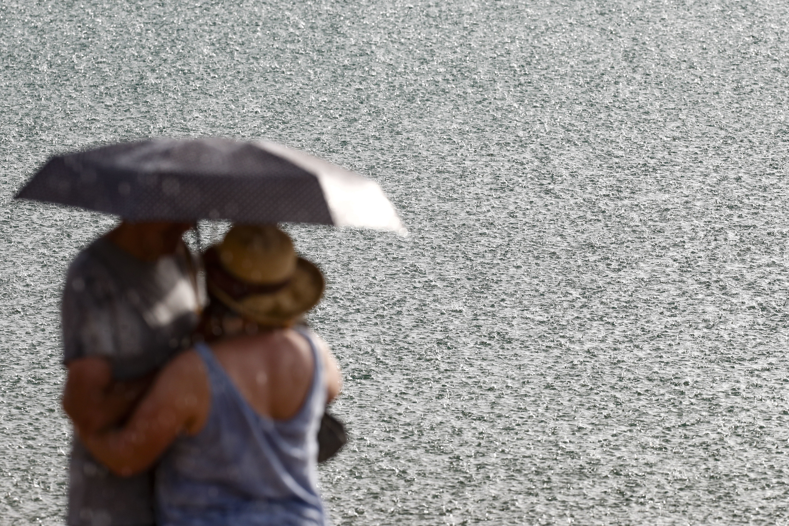 Dos personas se resguardan de la lluvia  junto al estanque de la Tranquera en Carenas (Zaragoza).