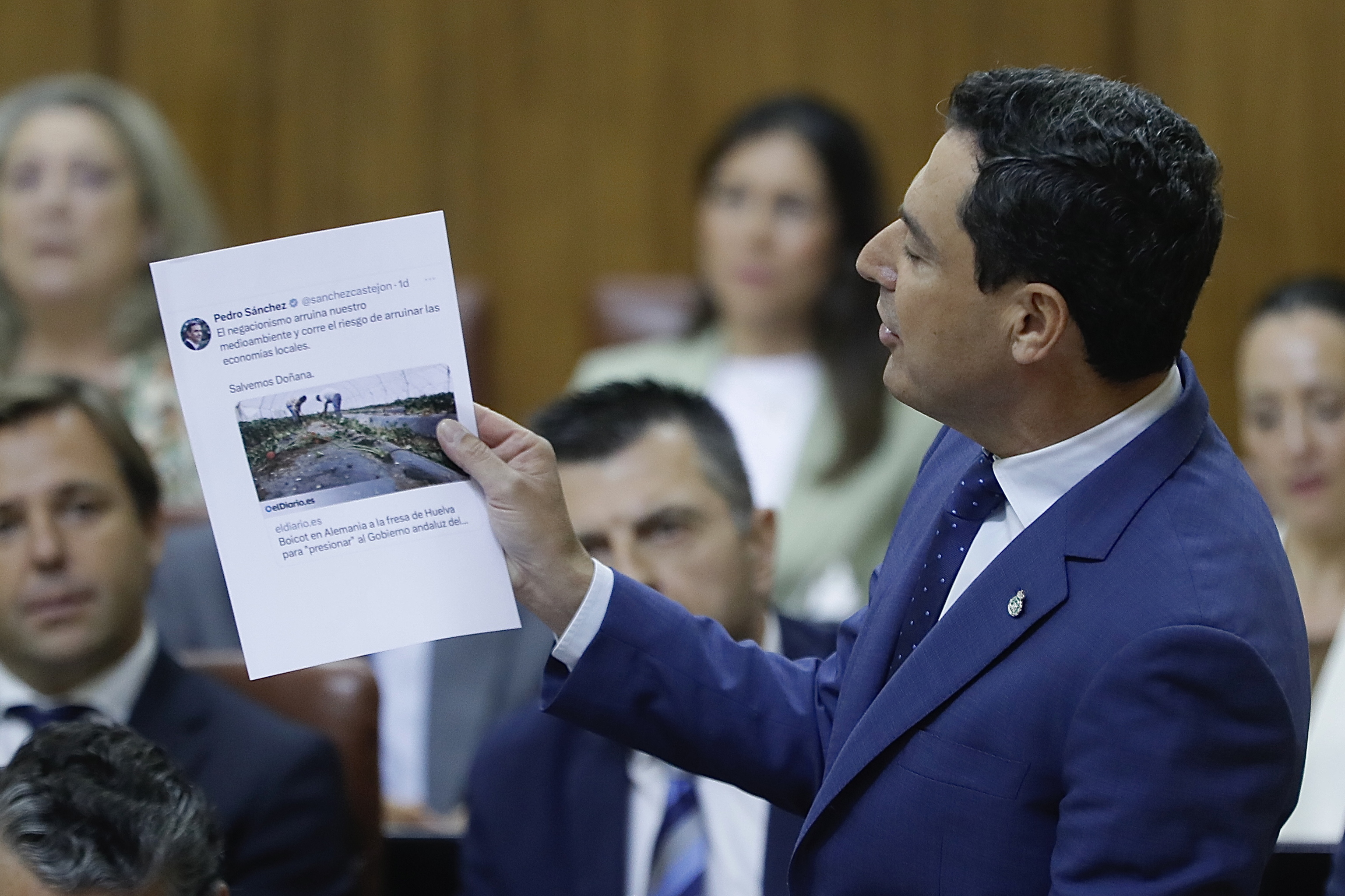 Juanma Moreno muestra unos titulares de prensa, durante su intervencin en el Parlamento.