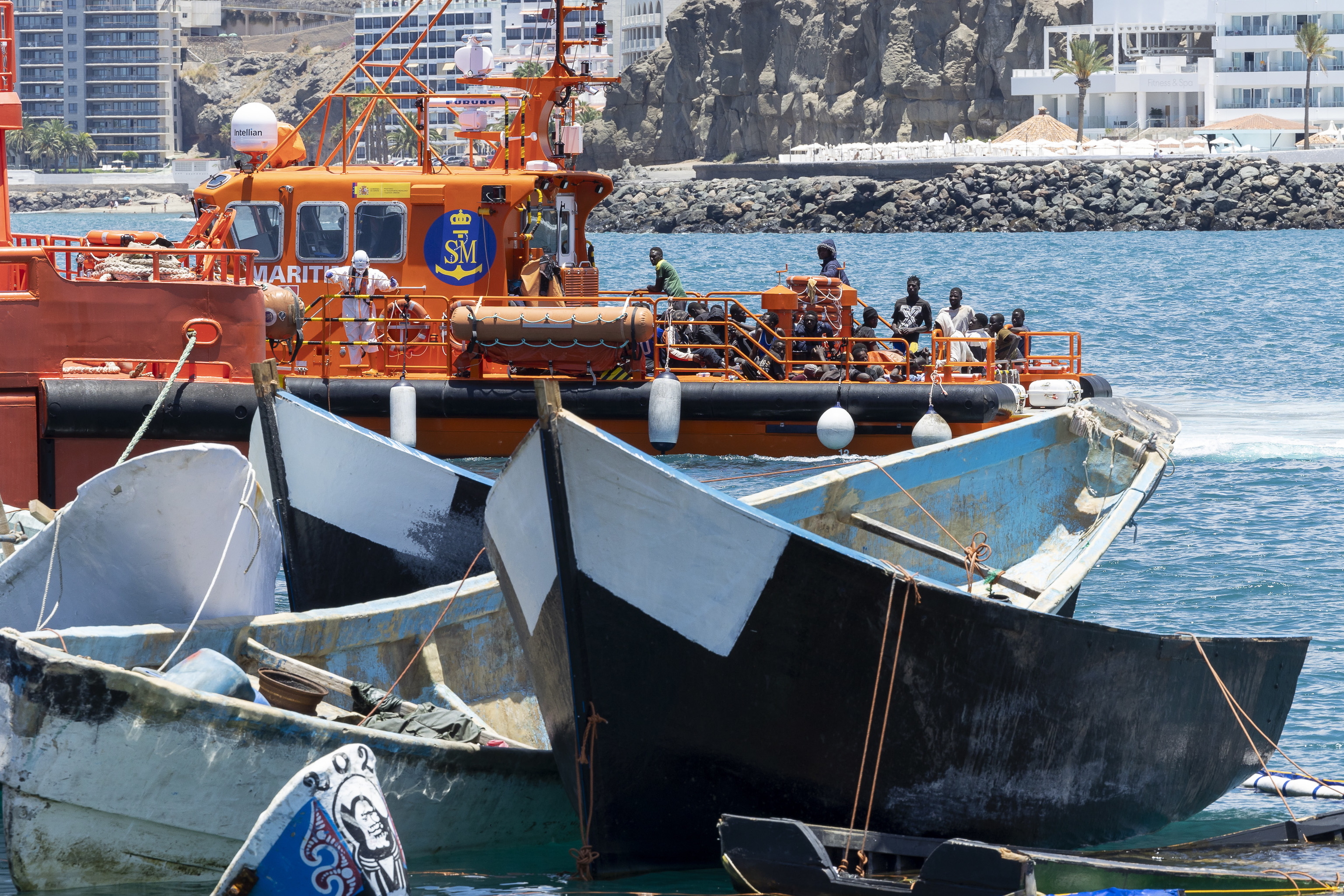Salvamento Martimo traslada a un grupo de inmigrantes al puerto de Arguinegun (Gran Canaria), al lado de pateras rescatadas en el pasado.